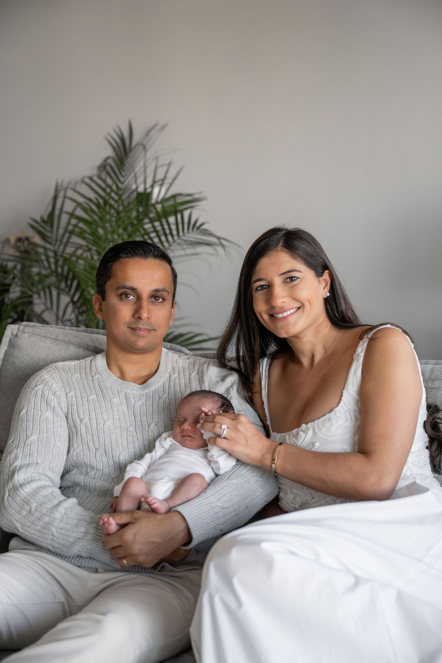 Family portrait on white bedding with newborn baby and parents in casual attire.