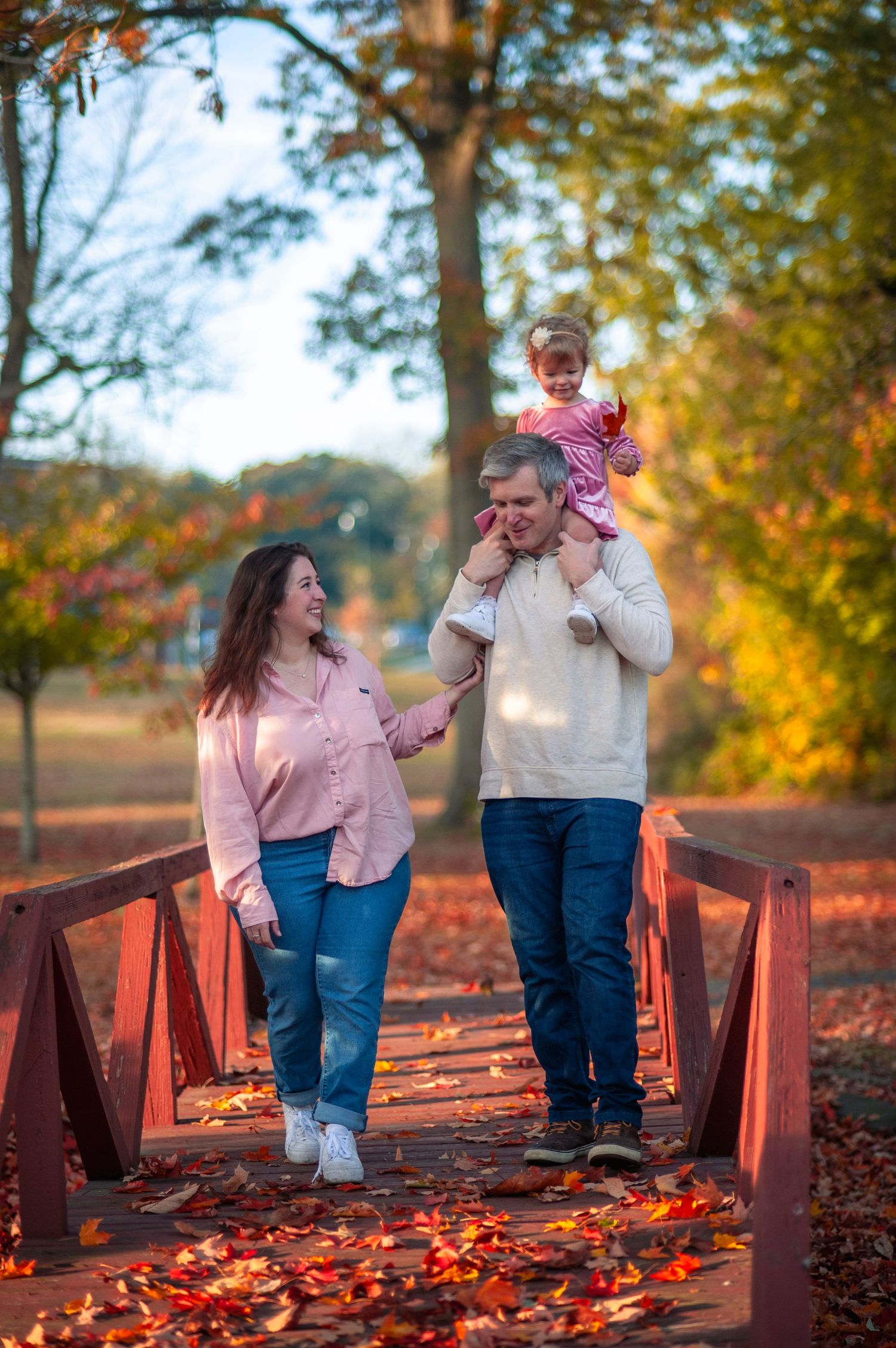Family walking together on a wooden bridge surrounded by vibrant autumn foliage.