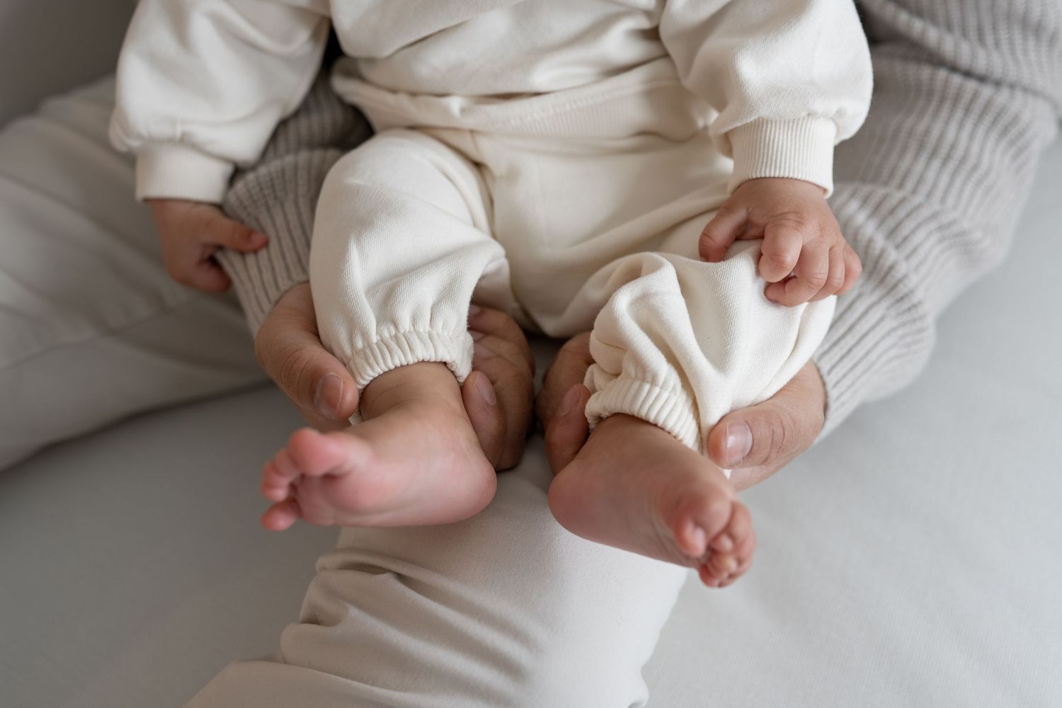 Close-up of newborn baby feet and legs in cream outfit resting on parent lap.