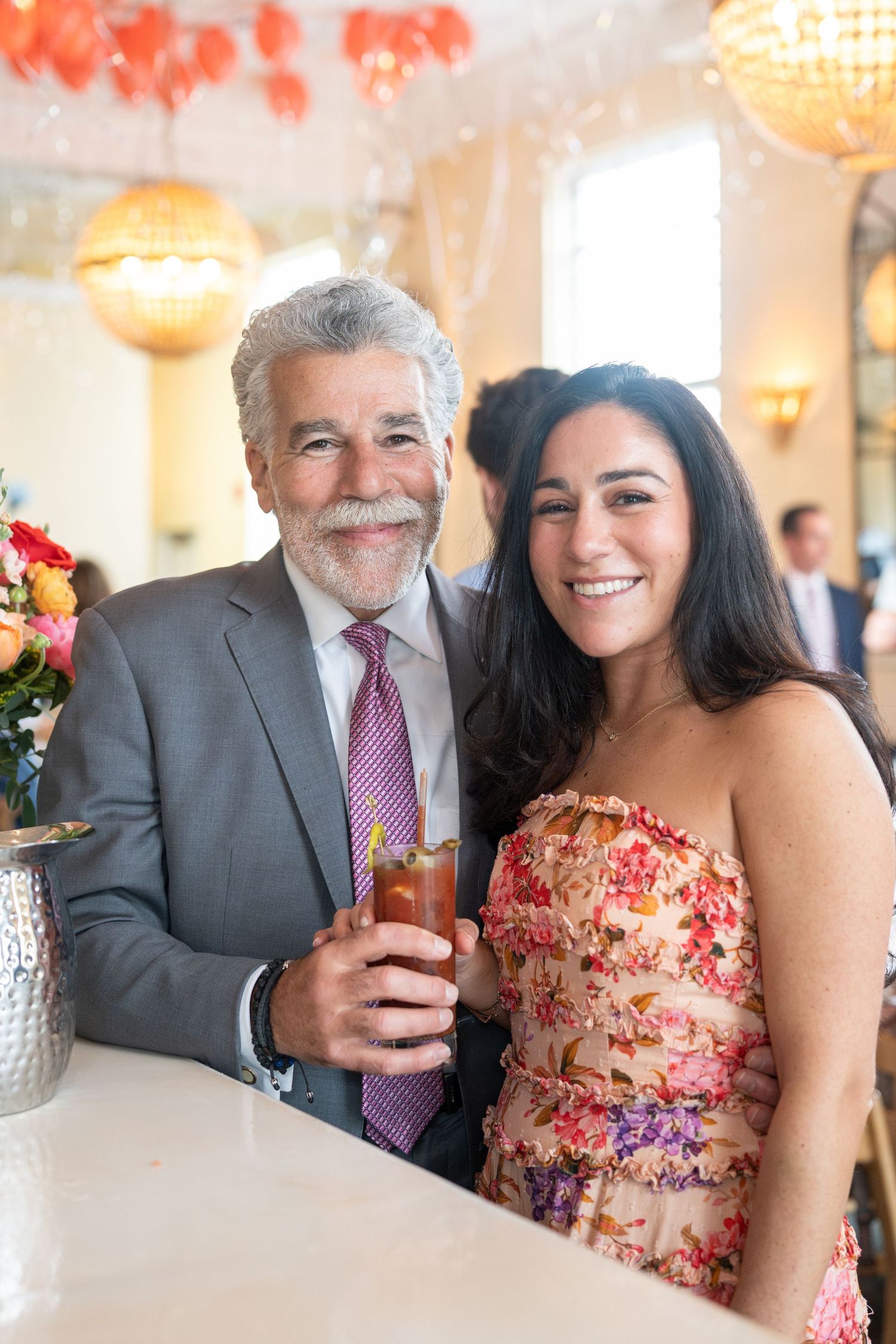 Older man with gray mustache and woman in floral dress smiling at restaurant celebration.