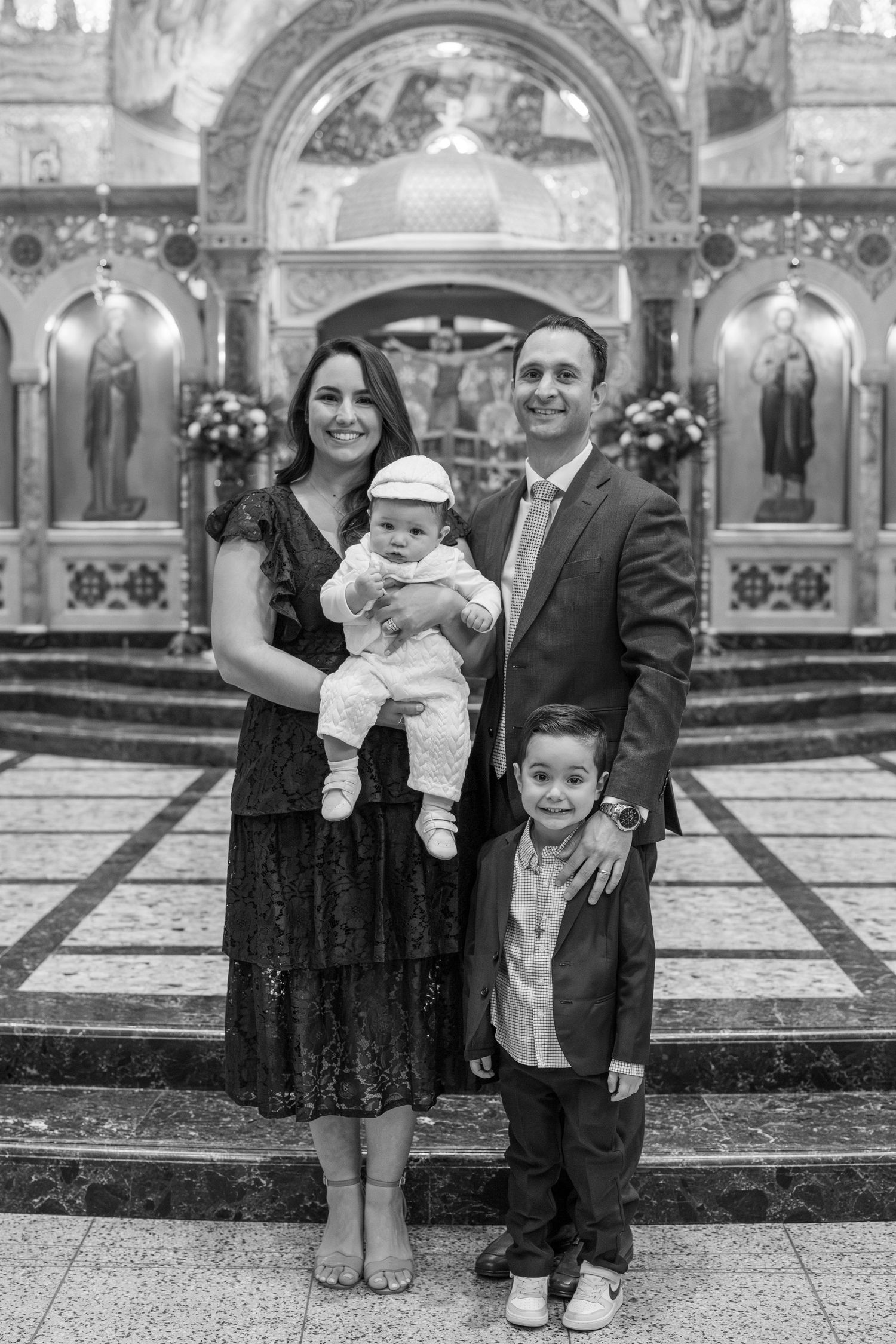 A family poses together for formal portraits during a baptism ceremony in a church setting.