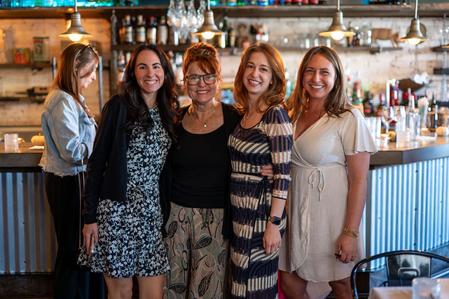 A group of friends smile together while gathered at a bar or restaurant interior.