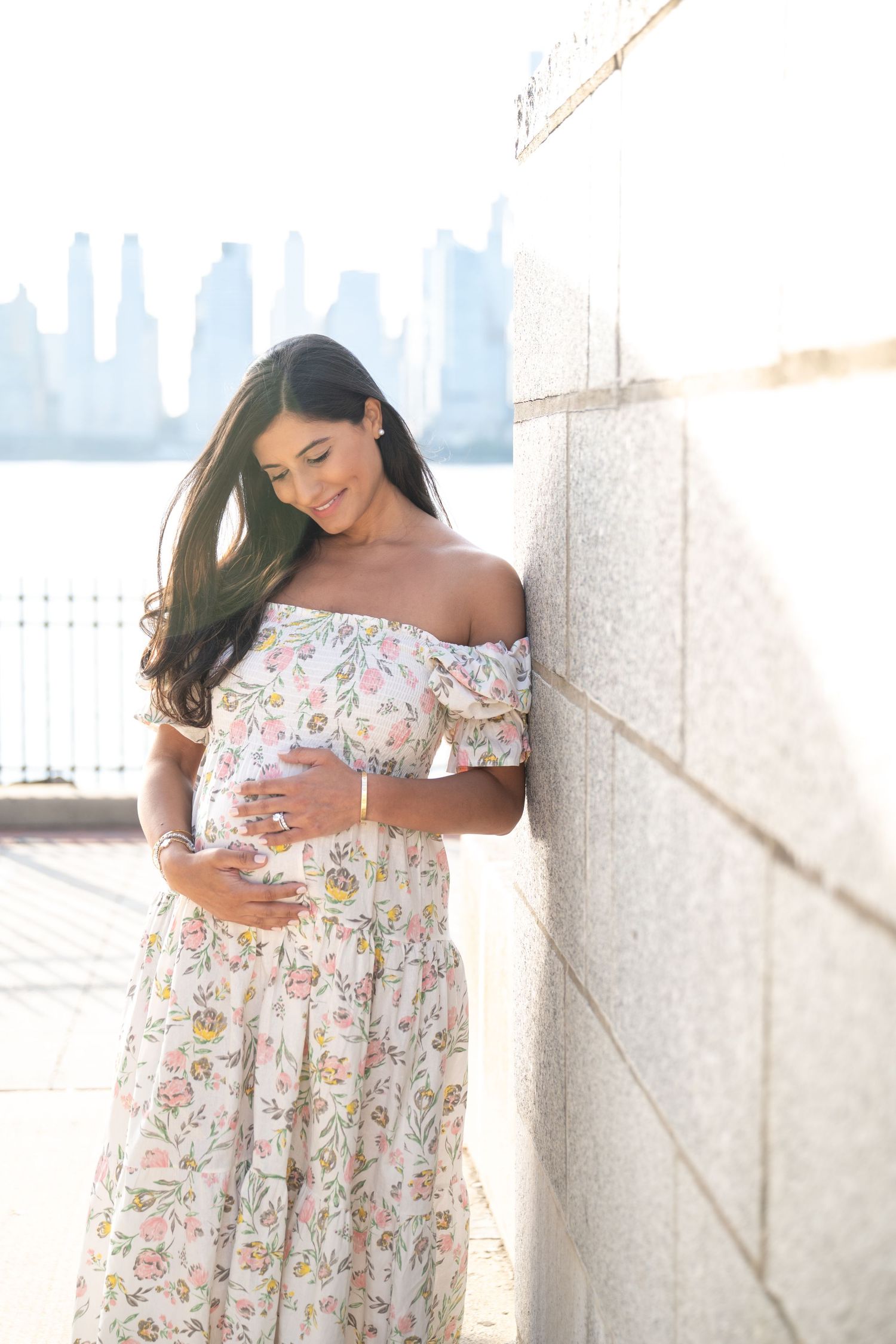 Maternity photos against stone wall with city skyline visible in background.