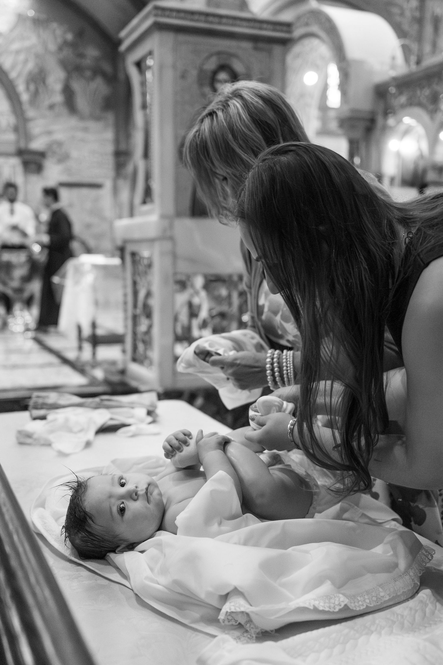 A black and white photo capturing an intimate moment during a religious baptism ceremony.