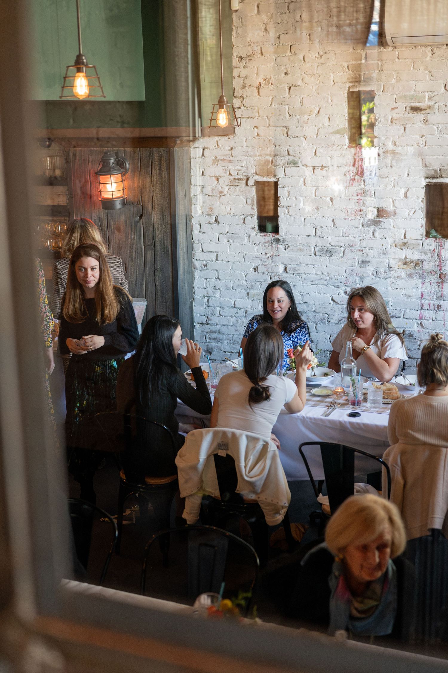 Interior of a rustic restaurant with exposed brick walls and pendant lighting during a social gathering.