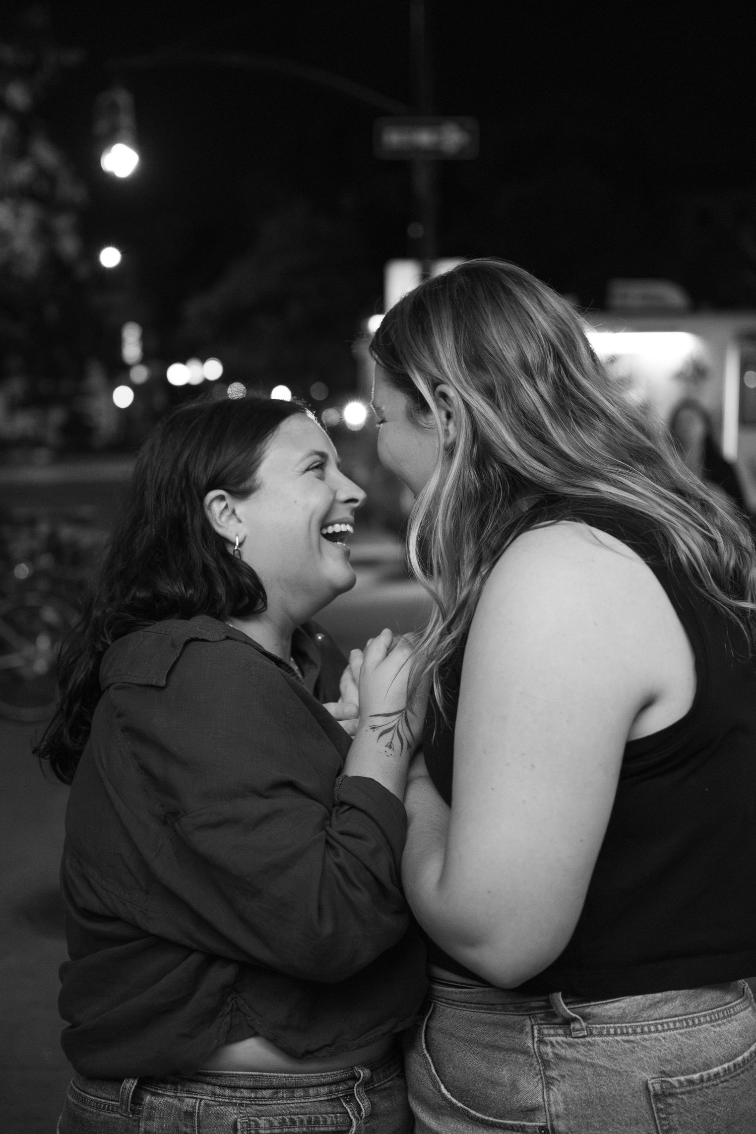 A black and white photo series captures two people sharing intimate laughter and joyful moments together outdoors at night.