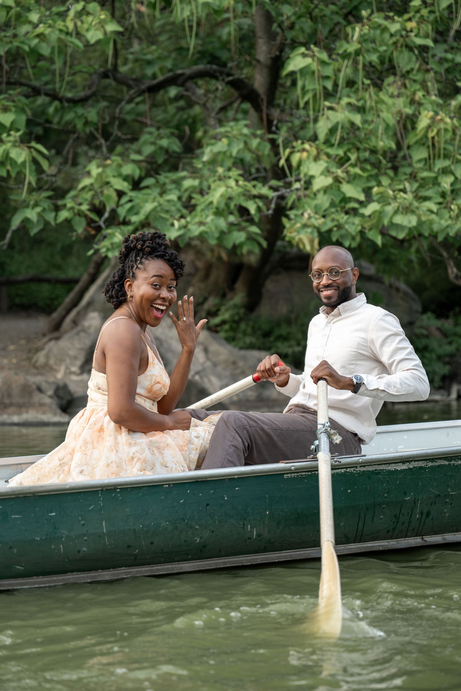 A couple relaxes together on a green canoe in a scenic lake surrounded by lush greenery.