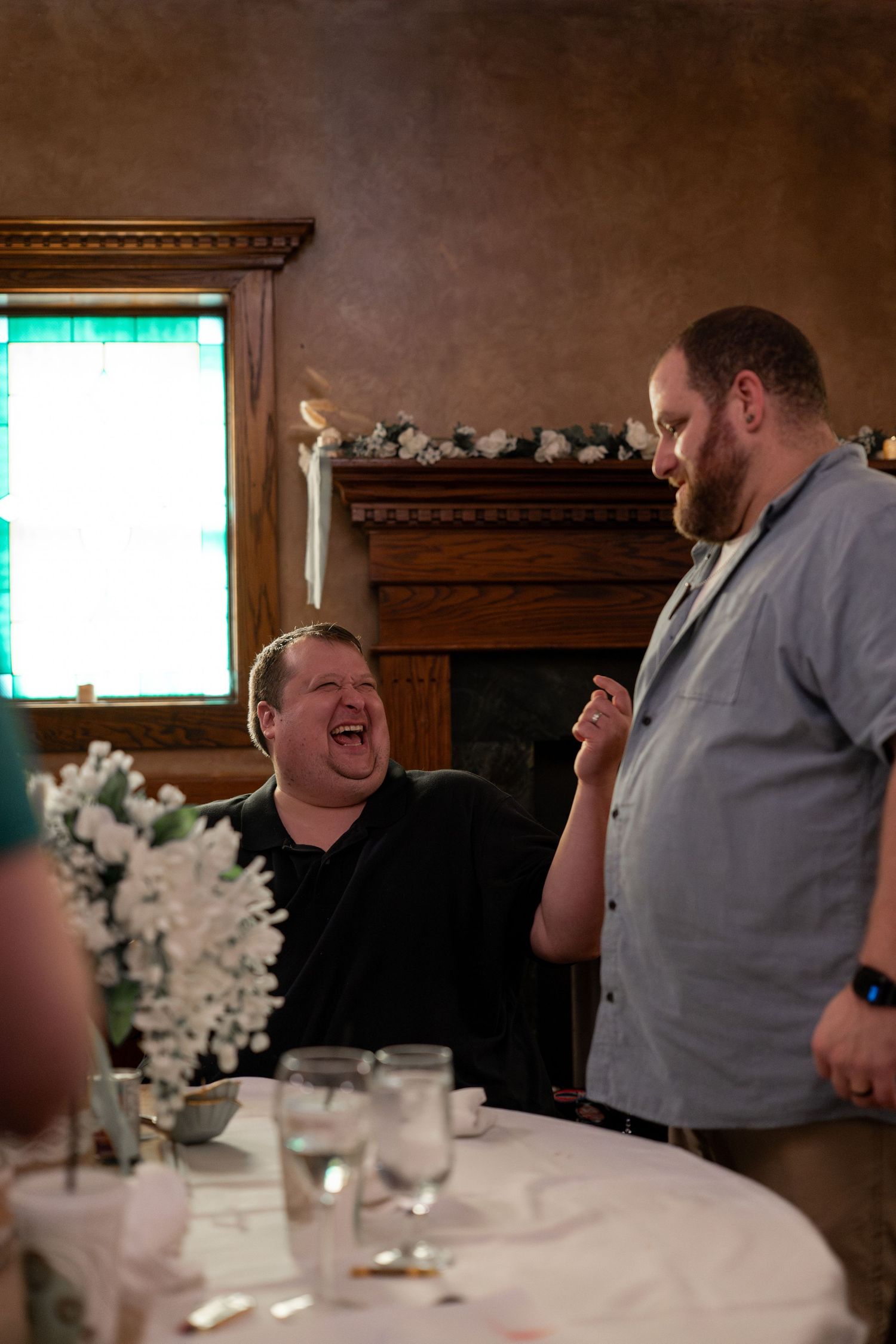 Two people sharing a laugh during a celebration dinner at an elegant venue with decorative lighting.