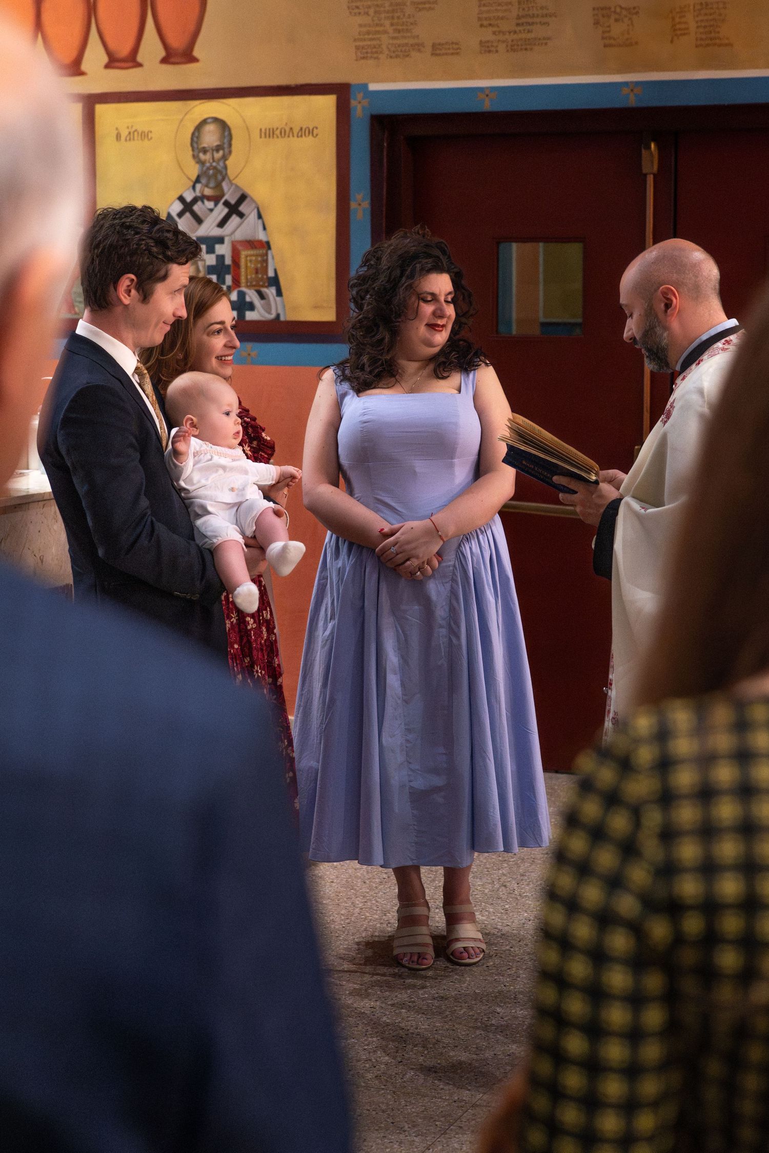 People in formal attire gather in a hallway, with someone wearing a light purple dress visible in the scene.