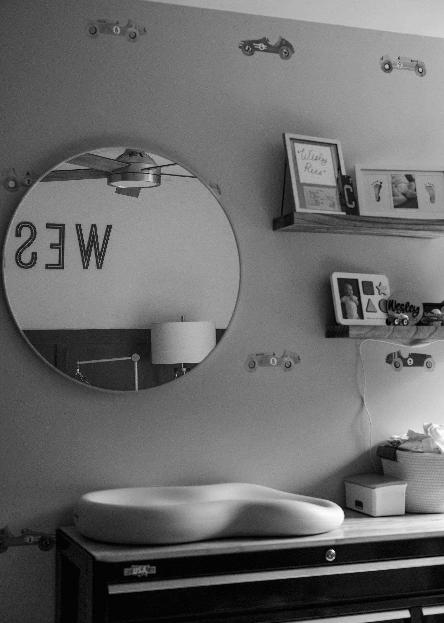 Vintage toy car models displayed on wall-mounted shelves in a black and white photograph.