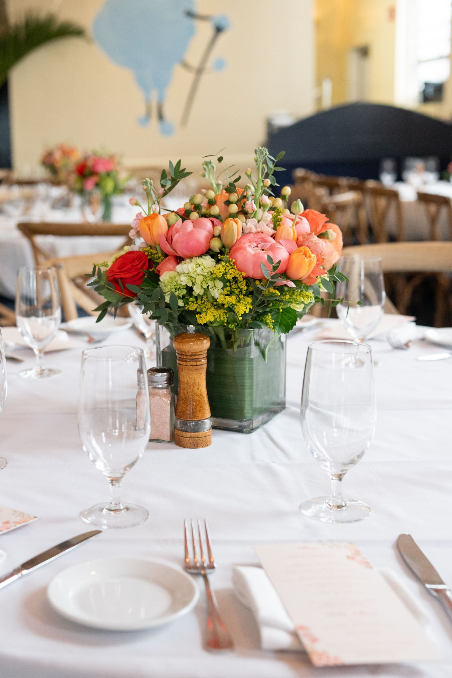 Colorful floral centerpiece with pink and red flowers on white tablecloth at wedding reception.