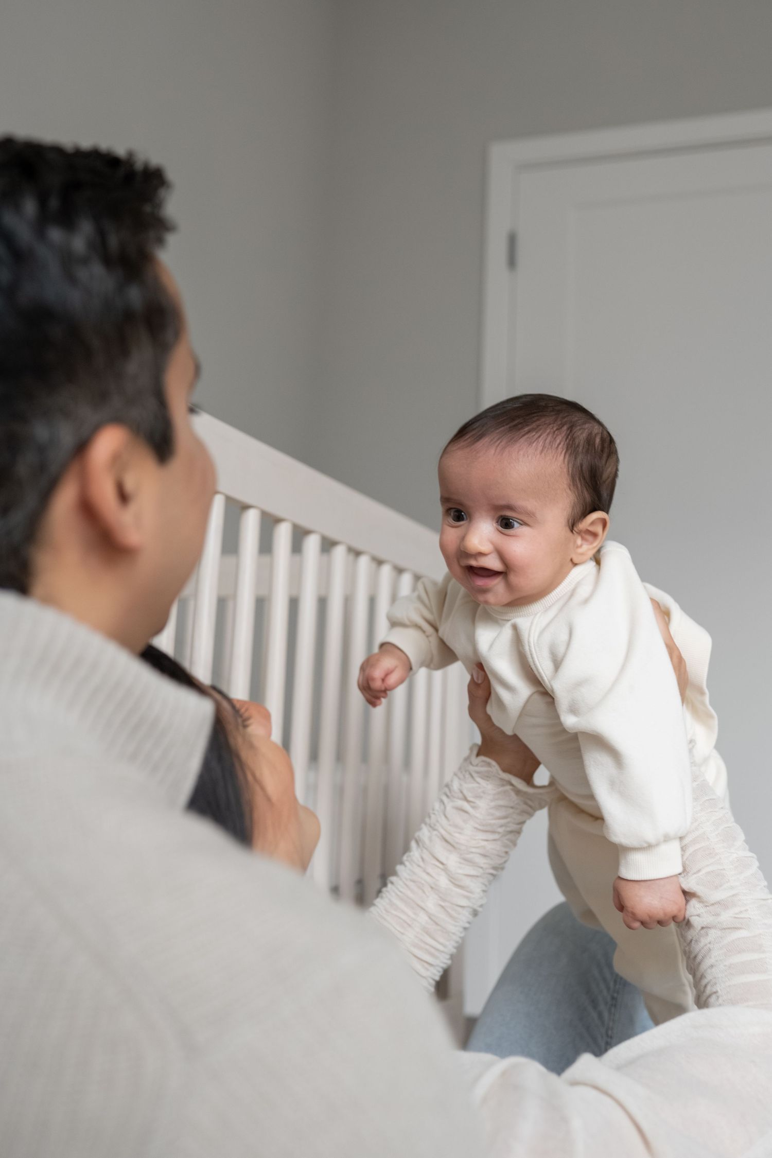 Father holding smiling baby near white crib in bright nursery room.