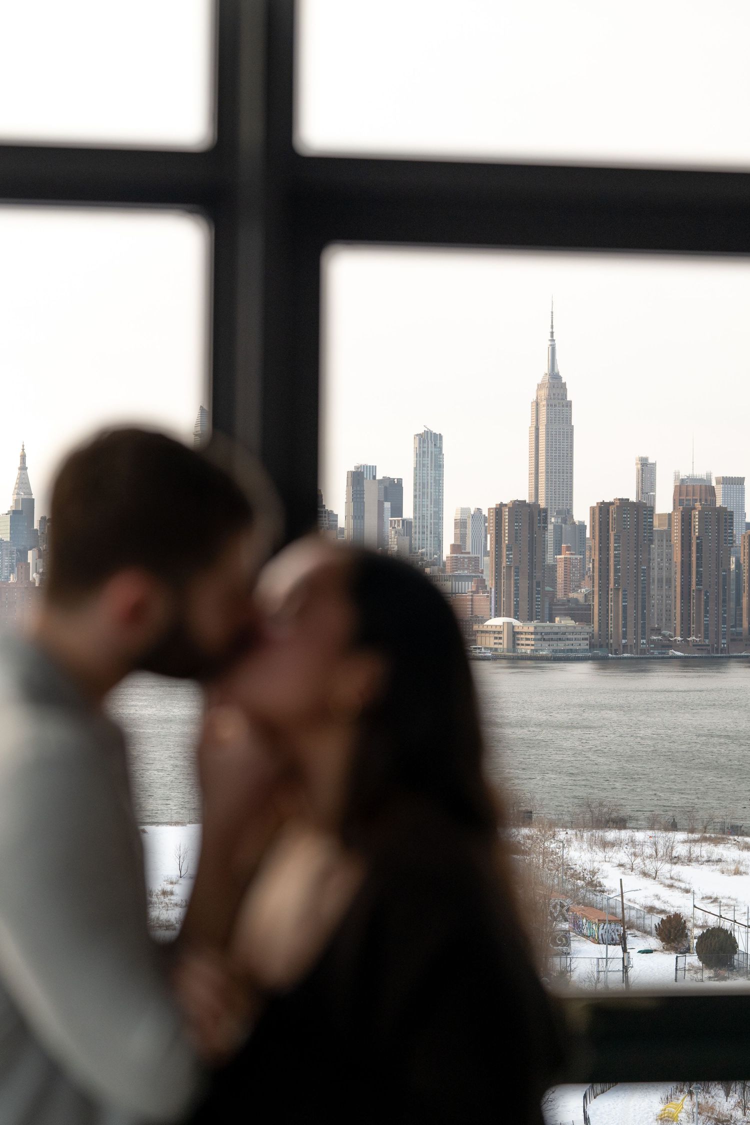 A romantic moment silhouetted against the New York City skyline visible through large windows.