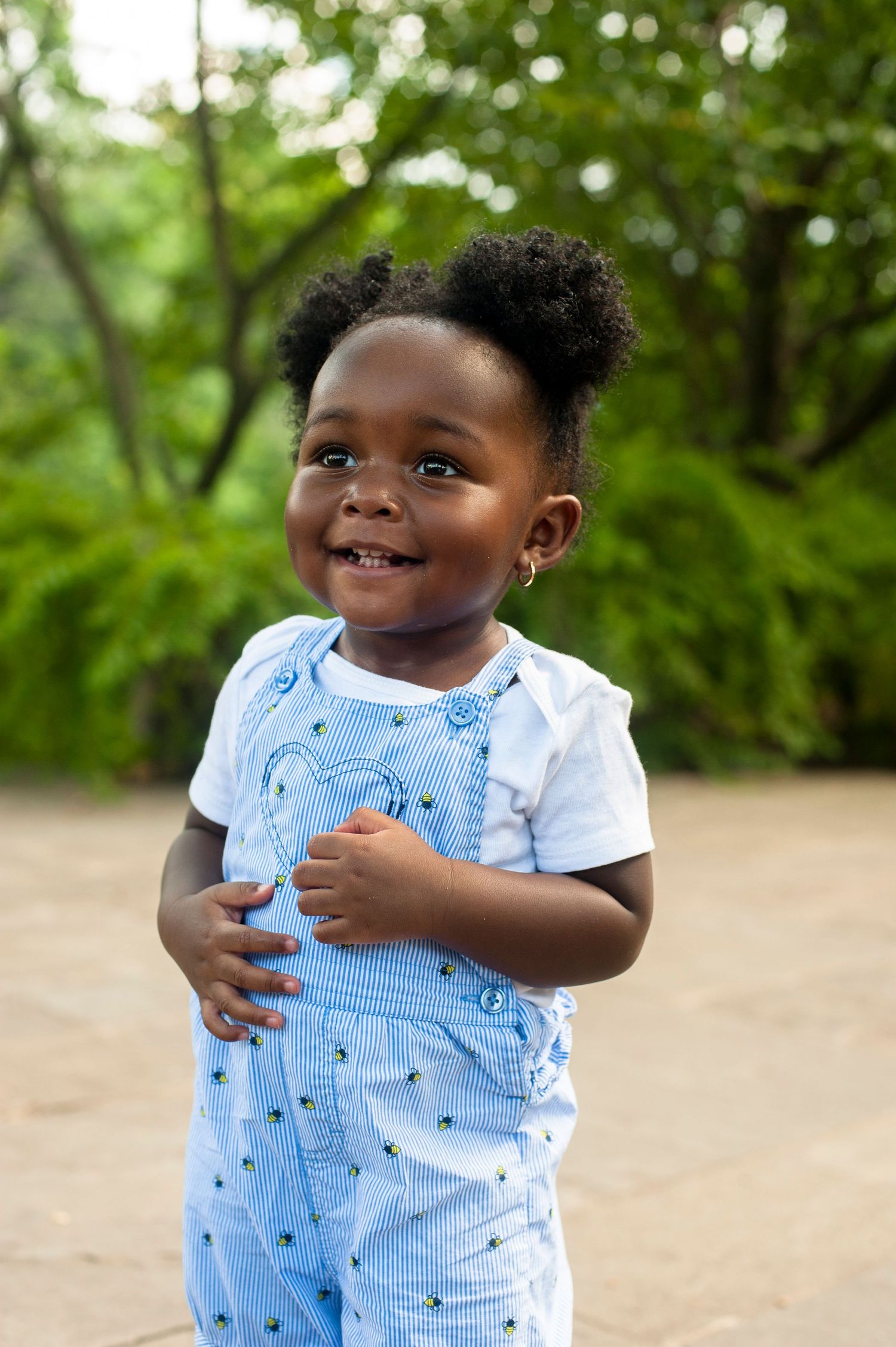 Toddler wearing light blue patterned outfit smiling and playing outdoors in a natural setting.