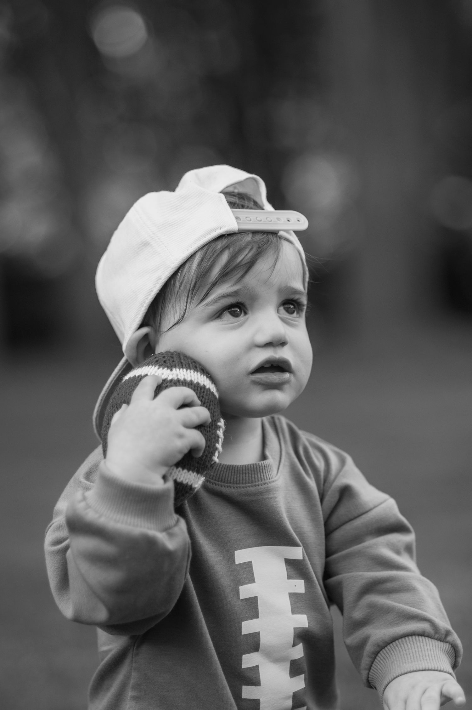 Black and white portrait of baby wearing football themed outfit and white cap.