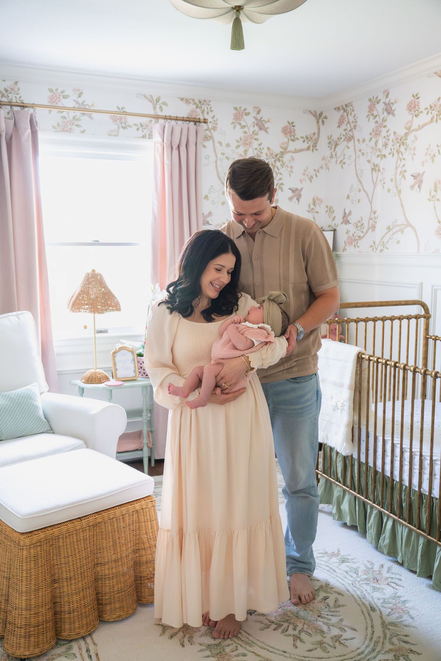 A nursery room decorated with floral wallpaper and pink curtains features a wooden crib.