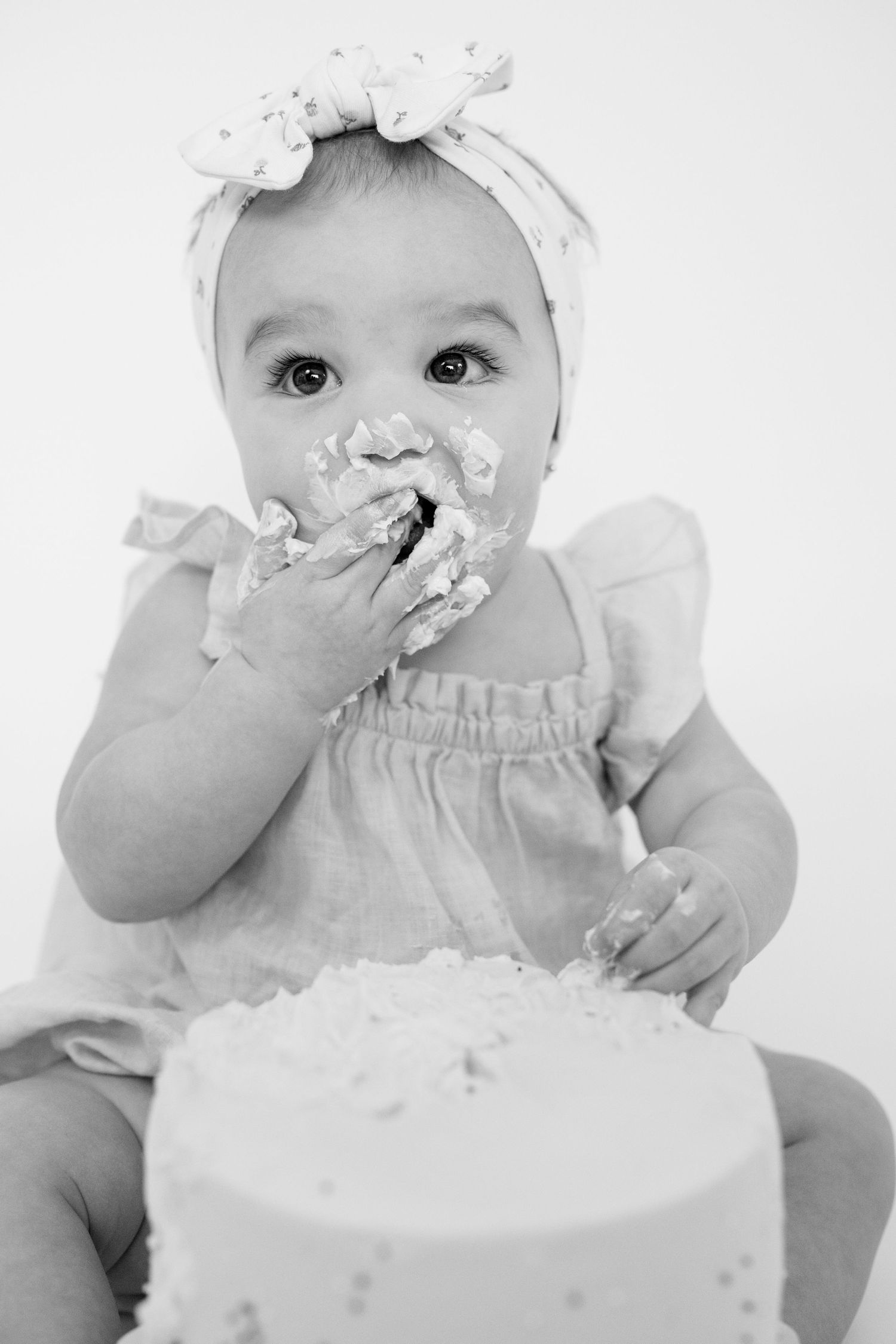 Black and white photos of baby enjoying cake smash session with white frosting.