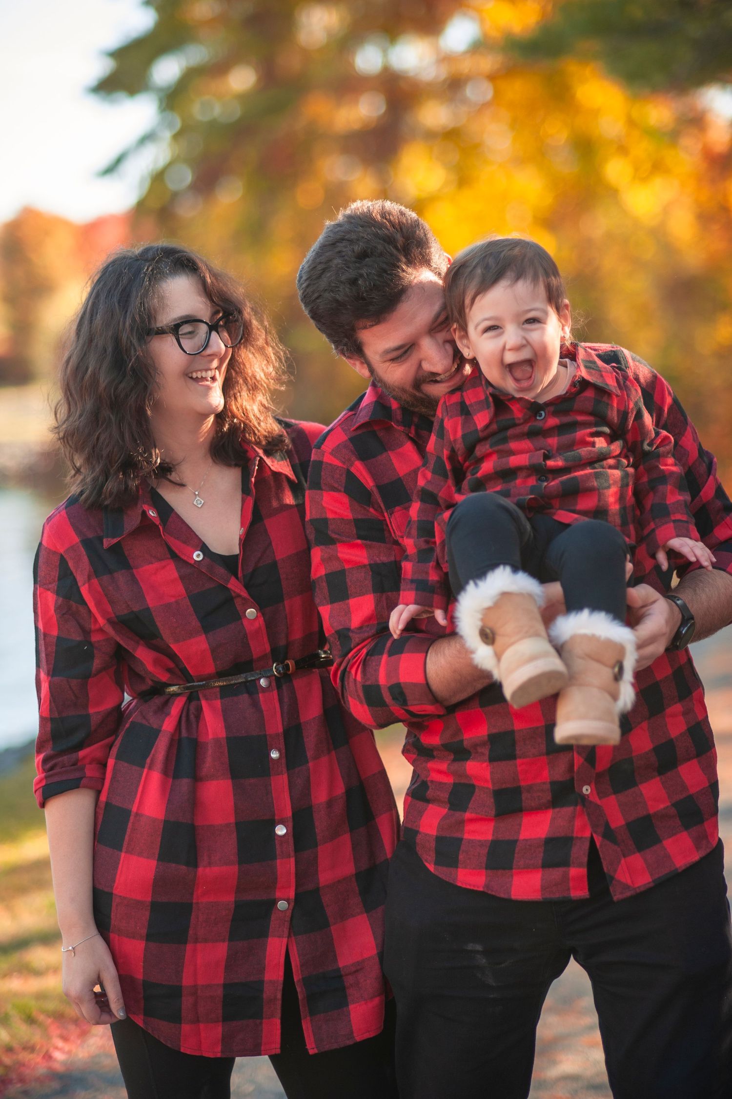 Family wearing matching buffalo plaid shirts sharing laughter during autumn photoshoot.