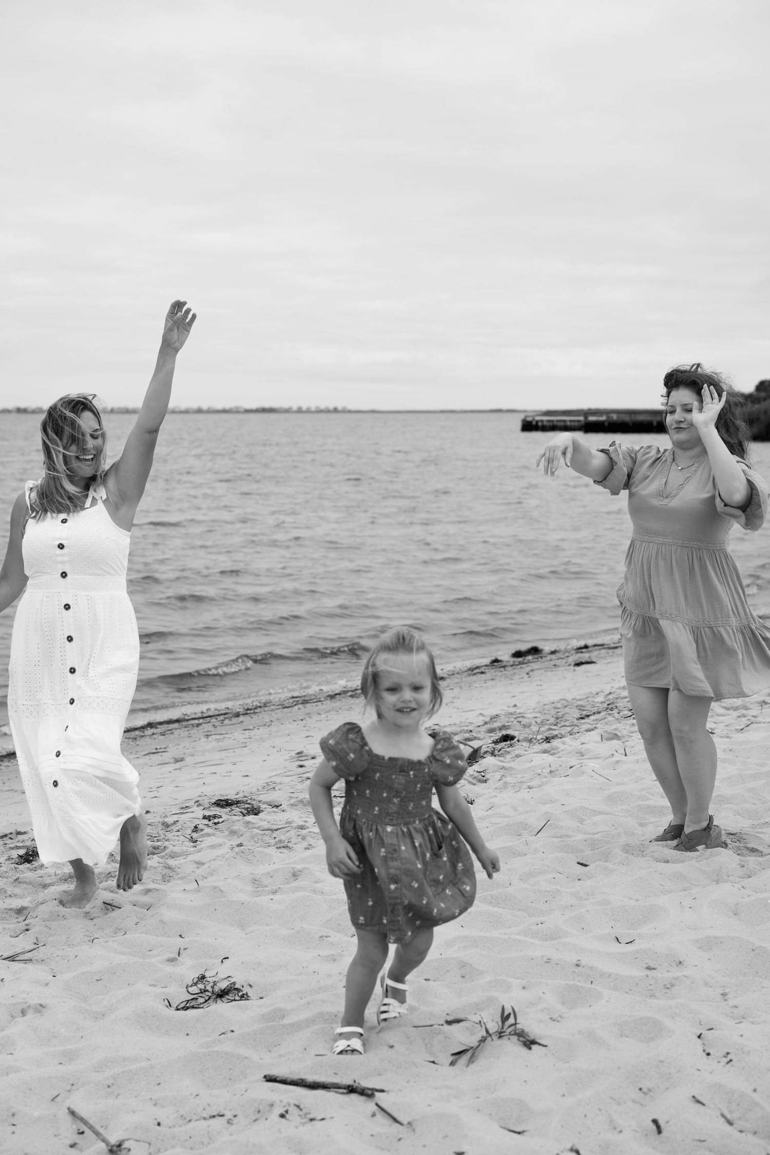 A series of playful moments captured on a beach showing joyful movement and dancing in black and white.