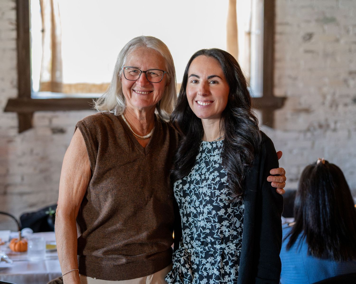 People gathered in a rustic brick-walled space sharing warm embraces and smiles during a social occasion.