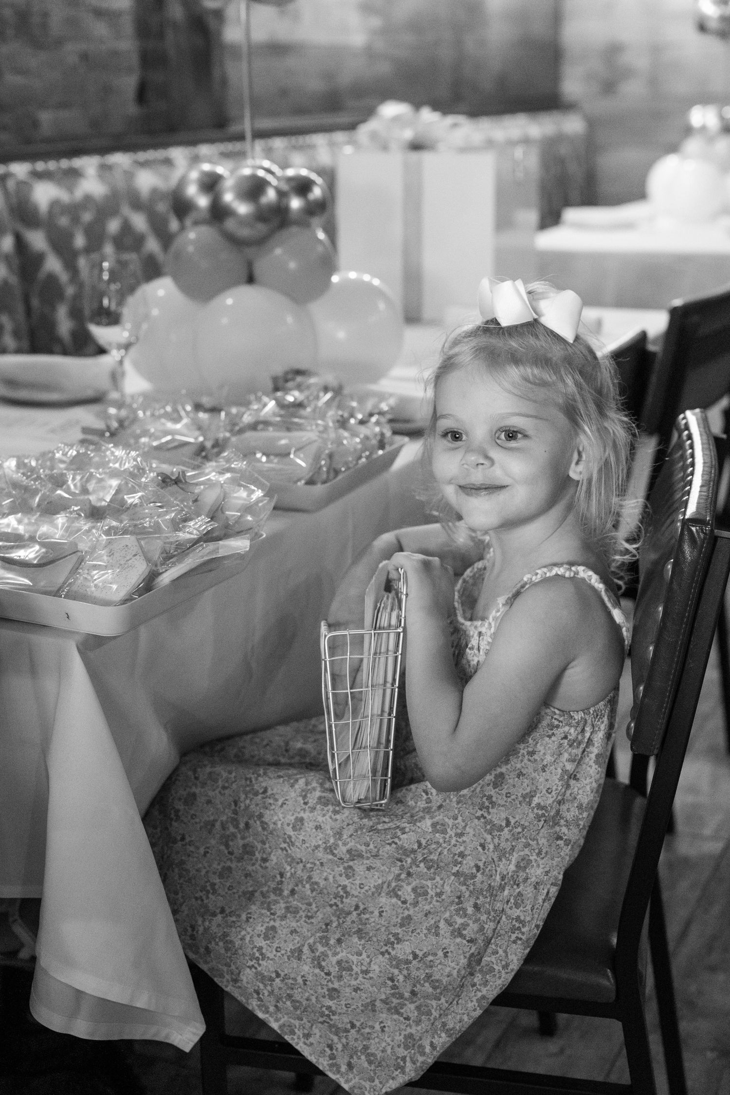 Young girl in a floral dress resting at a reception table with glassware.