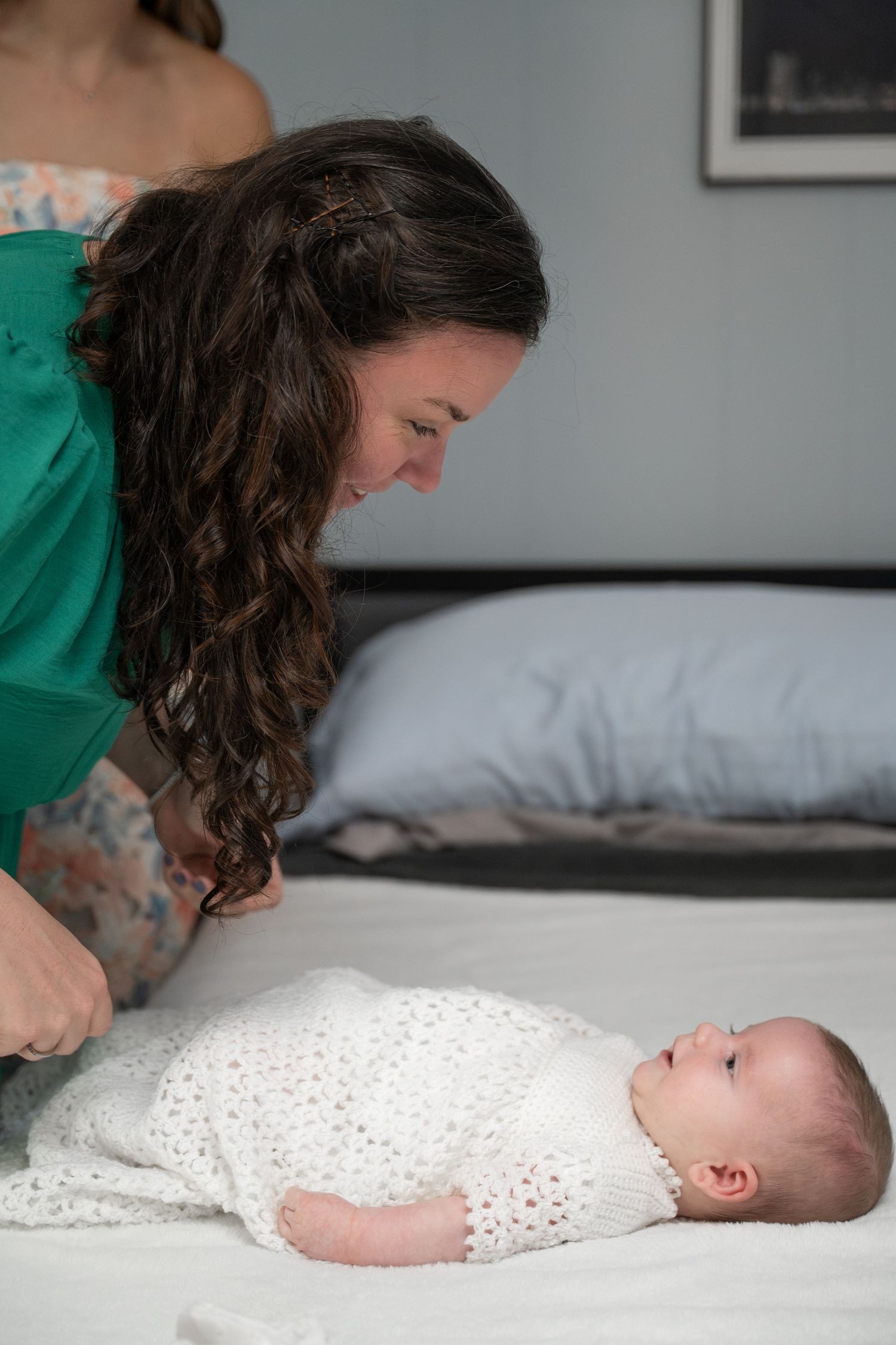A tender moment captured in a series showing a parent leaning over a baby in white clothing on a bed.