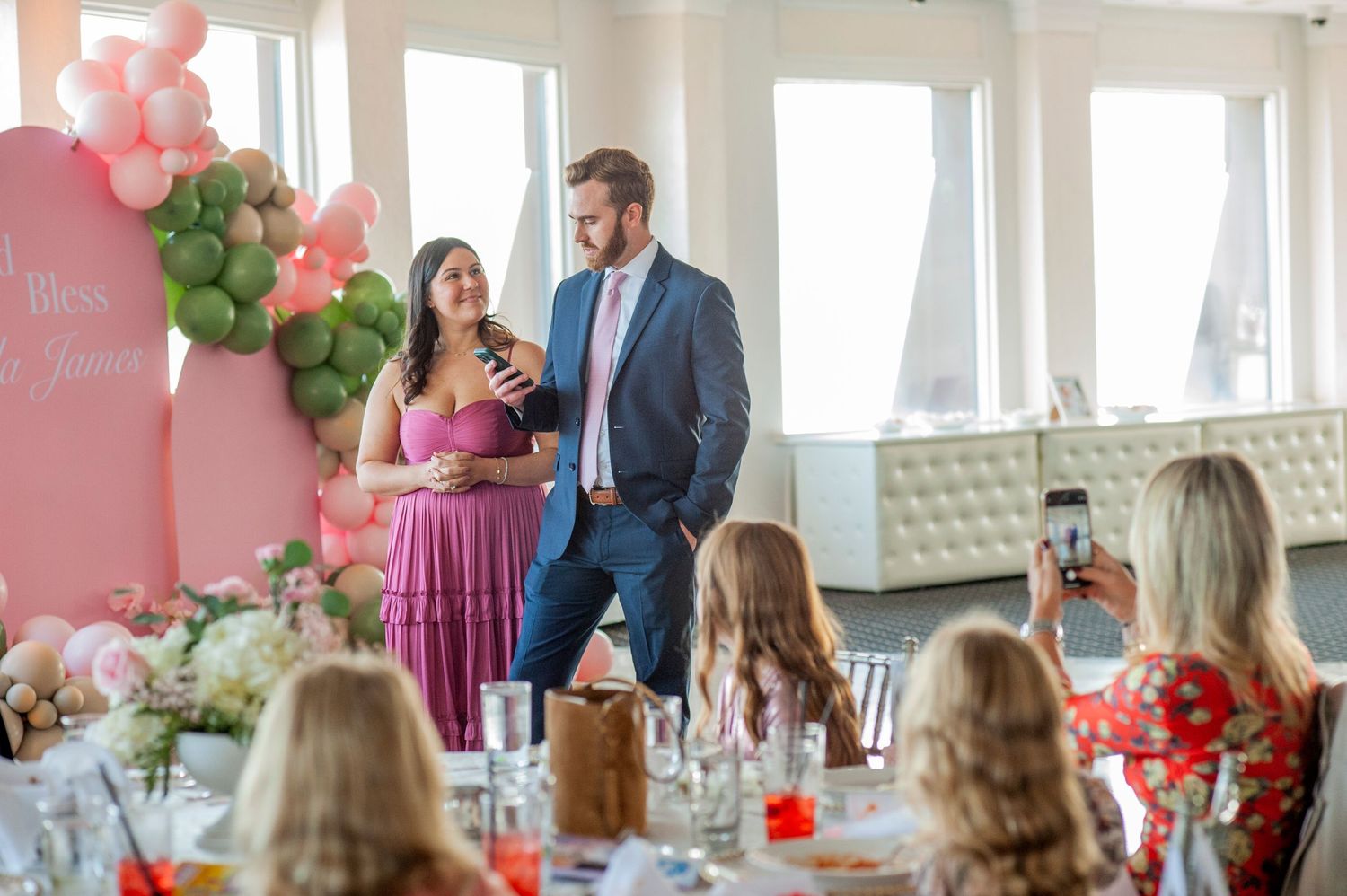 Celebration space decorated with pink and green balloons and guests seated at tables.