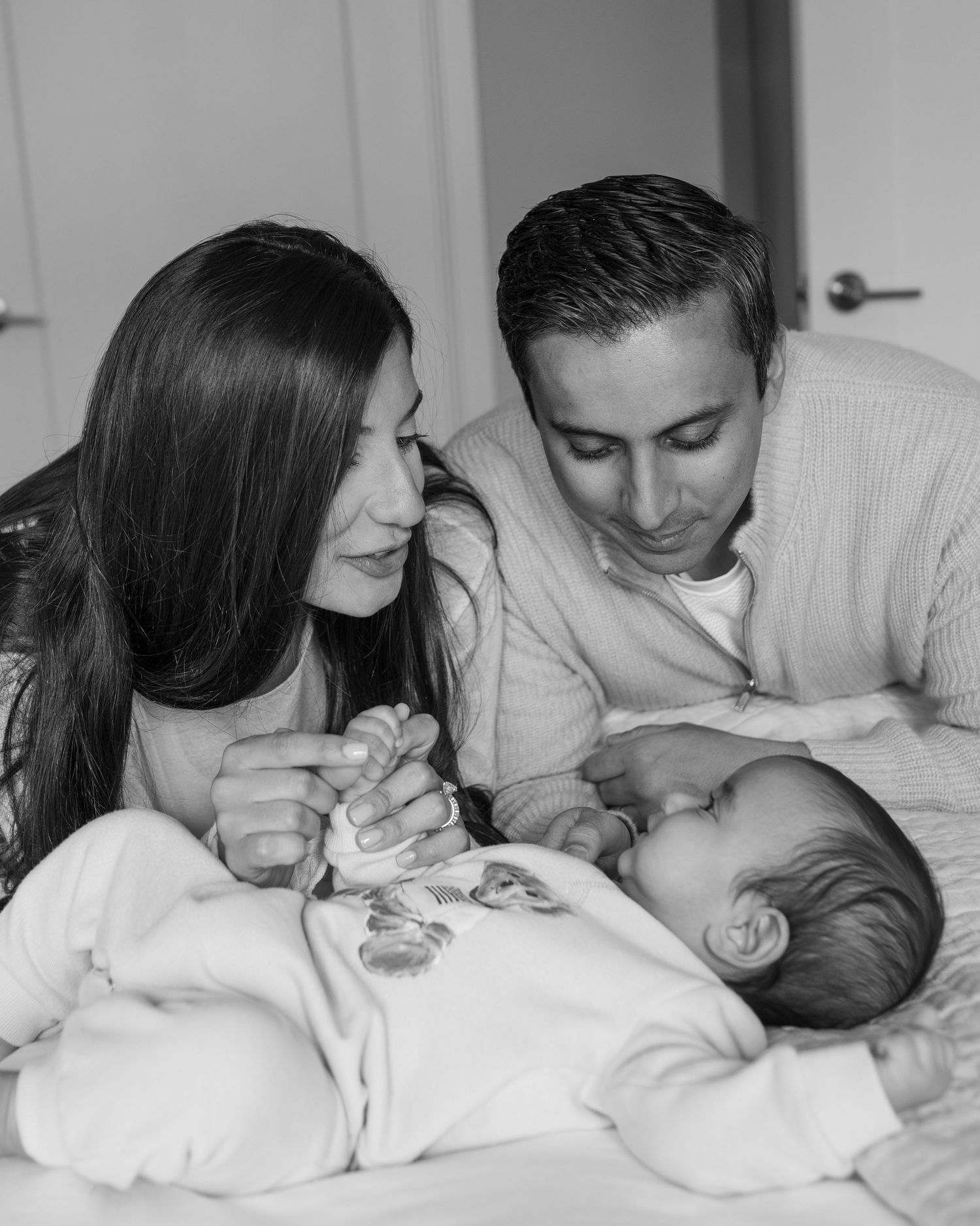Black and white photo of parents gazing lovingly at newborn baby.