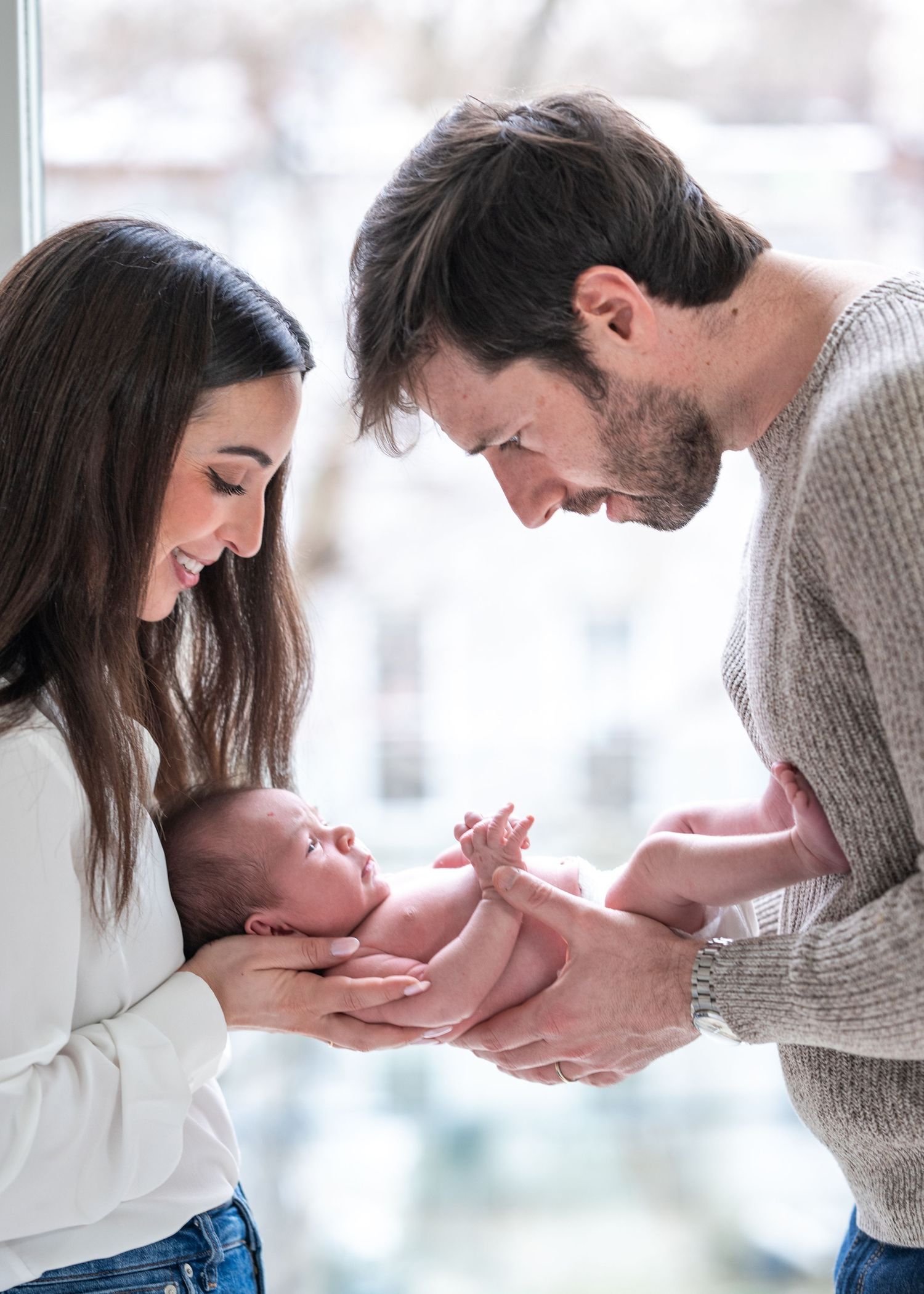 Parents gazing lovingly at their newborn baby while holding them together.
