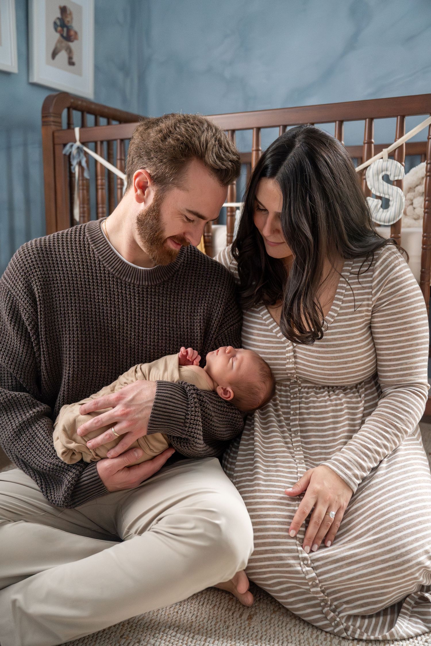 Parents in striped and brown sweaters lovingly bonding with their newborn on a bed.