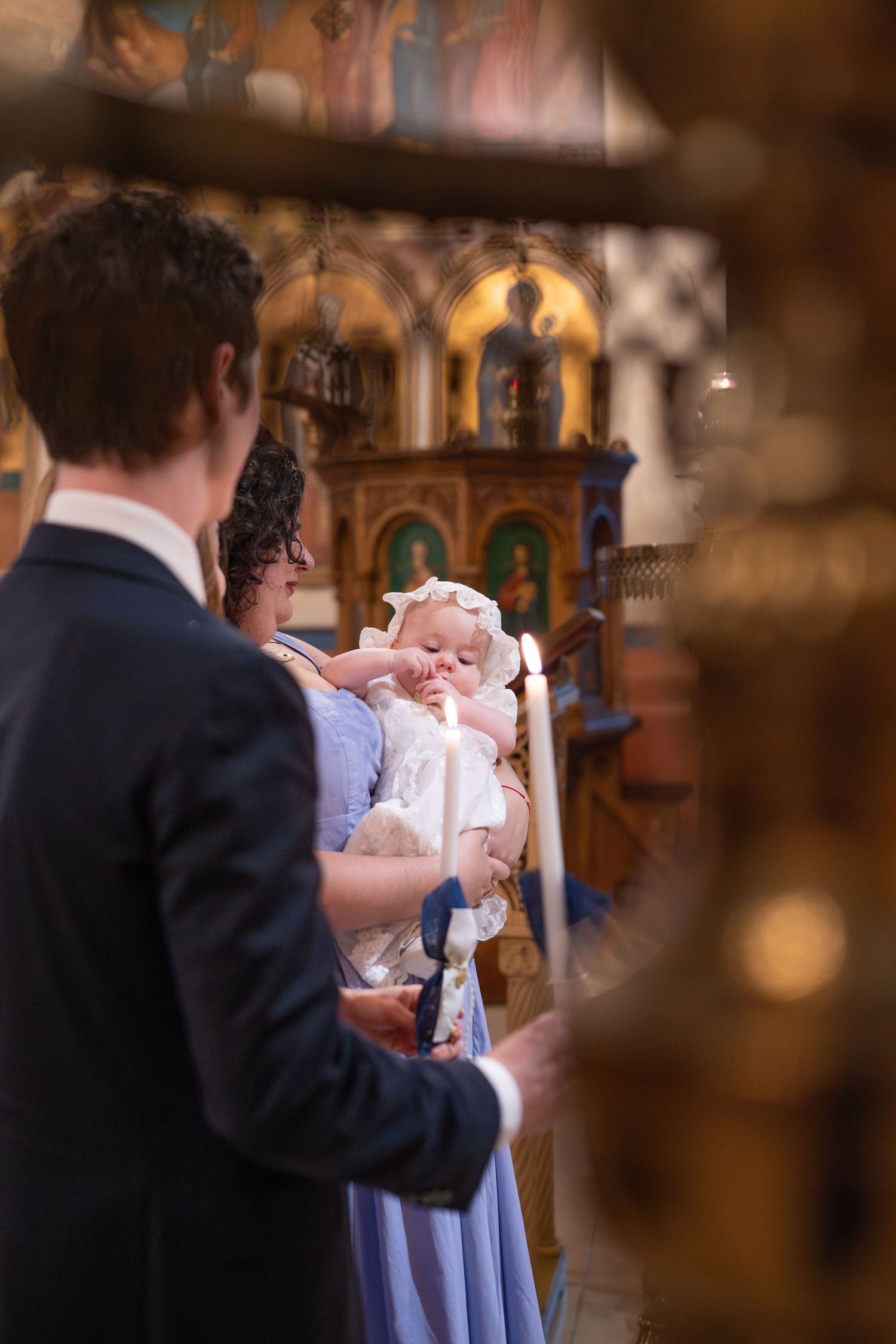 Church baptism ceremony viewed through decorative elements with attendees in formal attire.