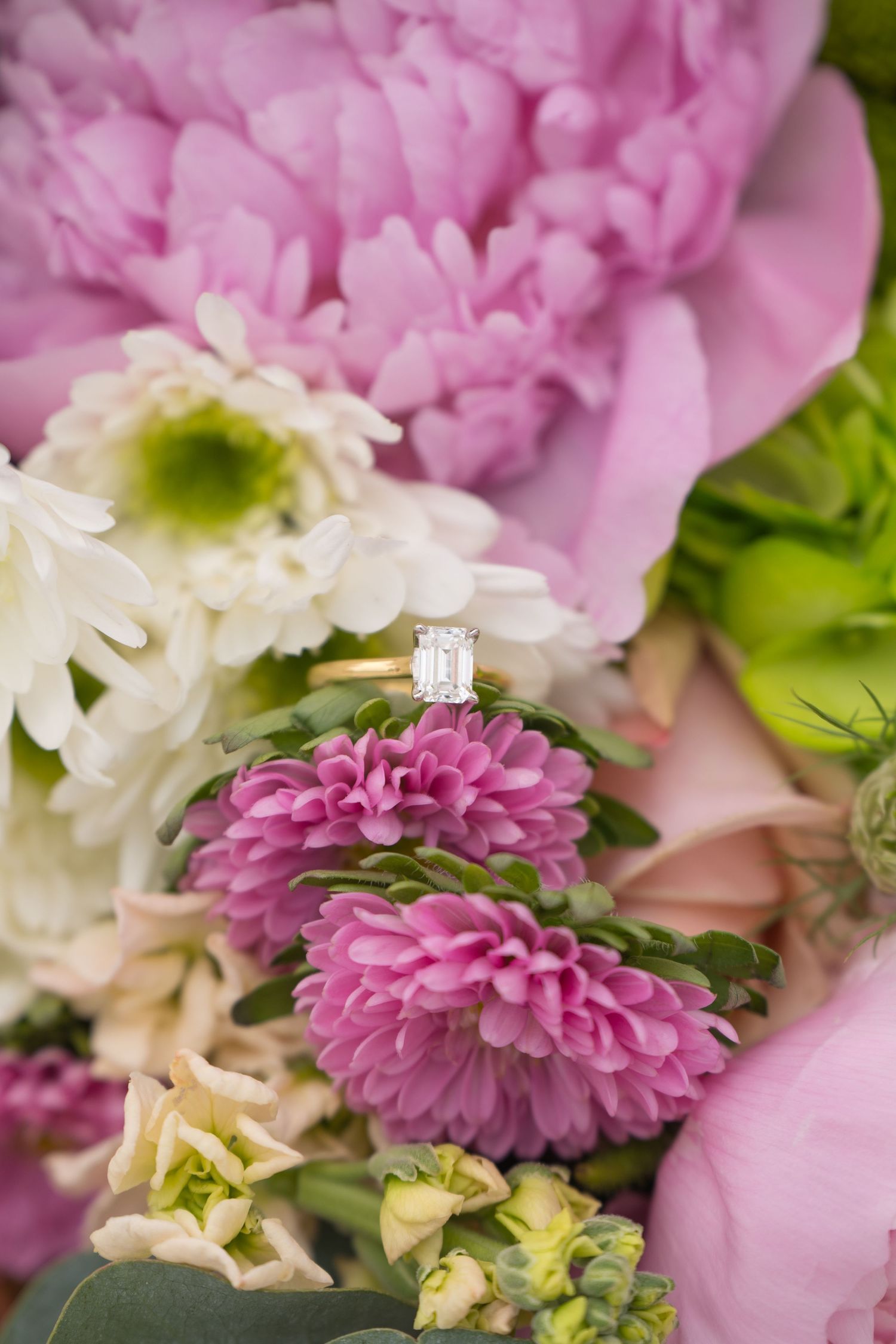 Diamond engagement ring displayed on pink and white flowers in a romantic floral arrangement.