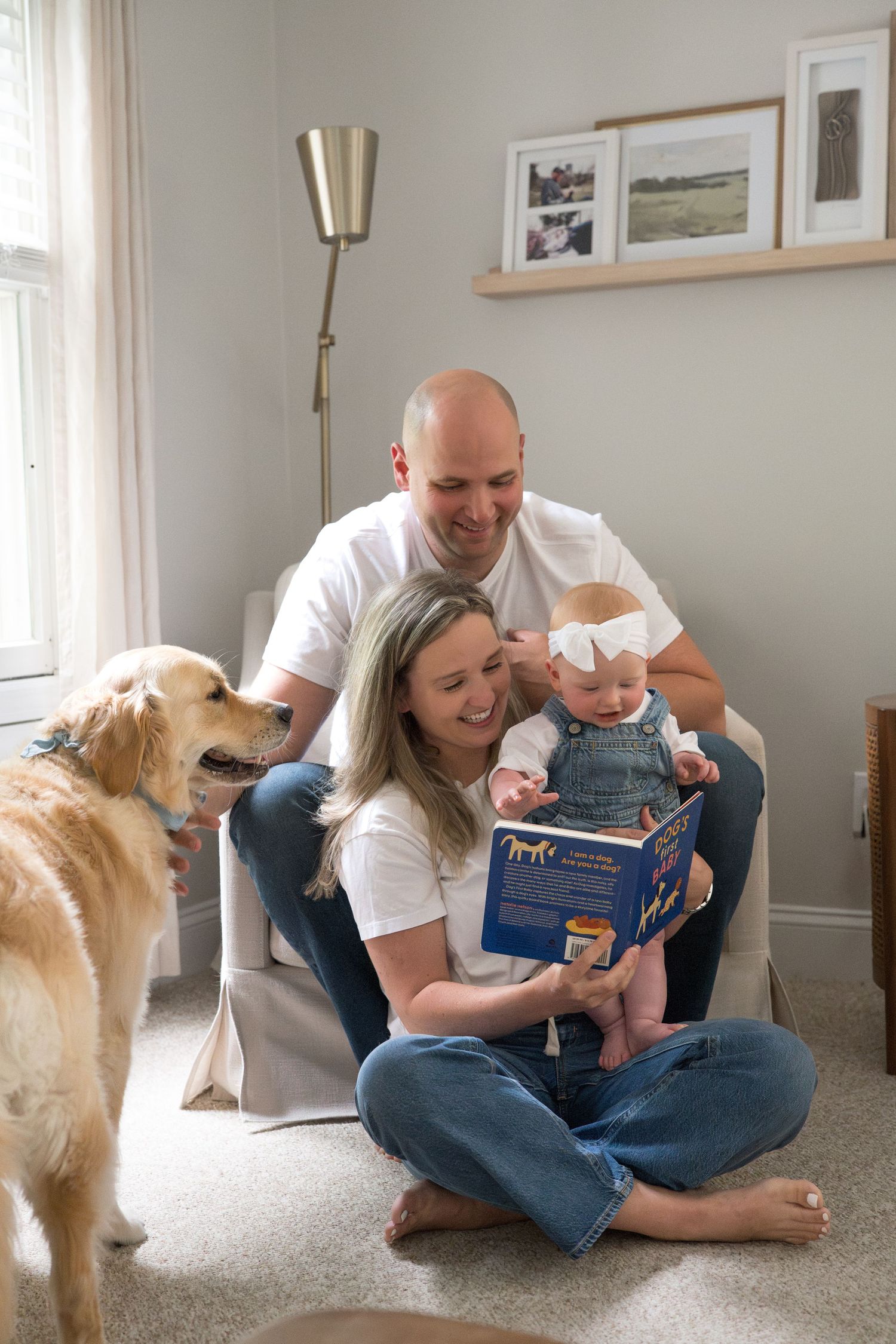A family reads a book together while sitting on the floor with their golden retriever nearby.