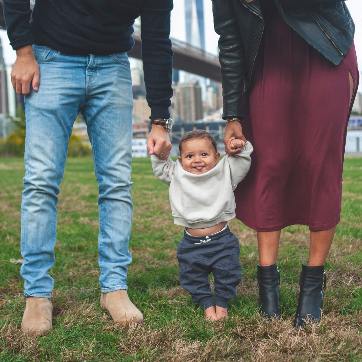 Row of feet and legs standing together on grass showing different footwear styles.