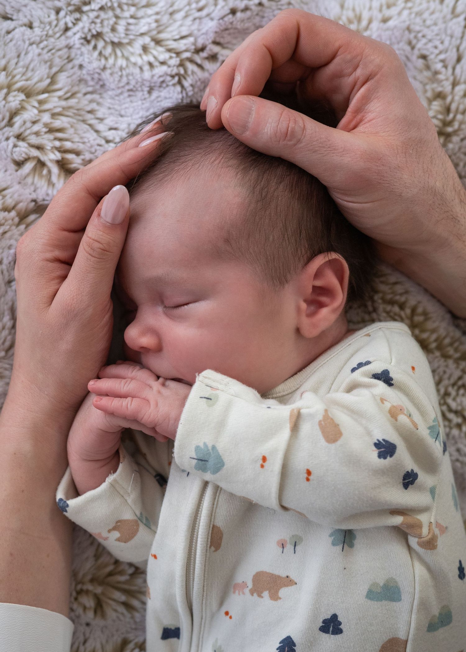 Close-up shots of a sleeping newborn wearing a patterned white onesie.