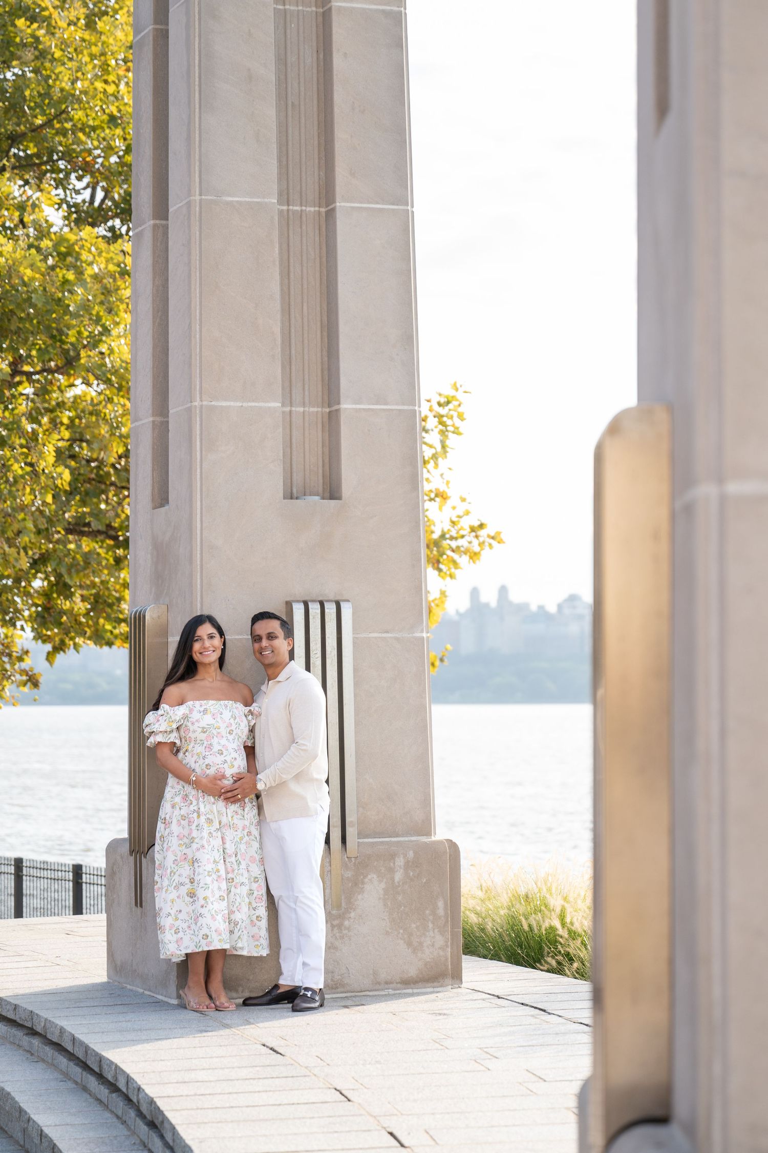 Romantic couple photos under architectural columns by waterfront during golden hour.