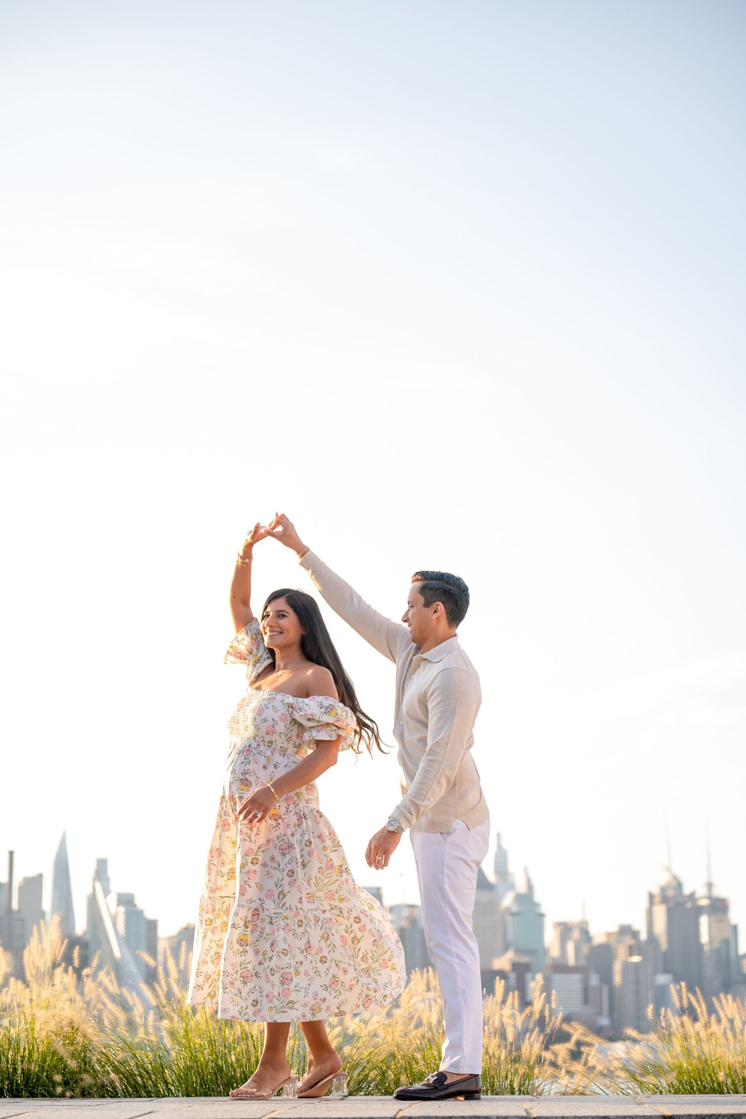 A couple dances together in a romantic sunset moment with a city skyline backdrop.