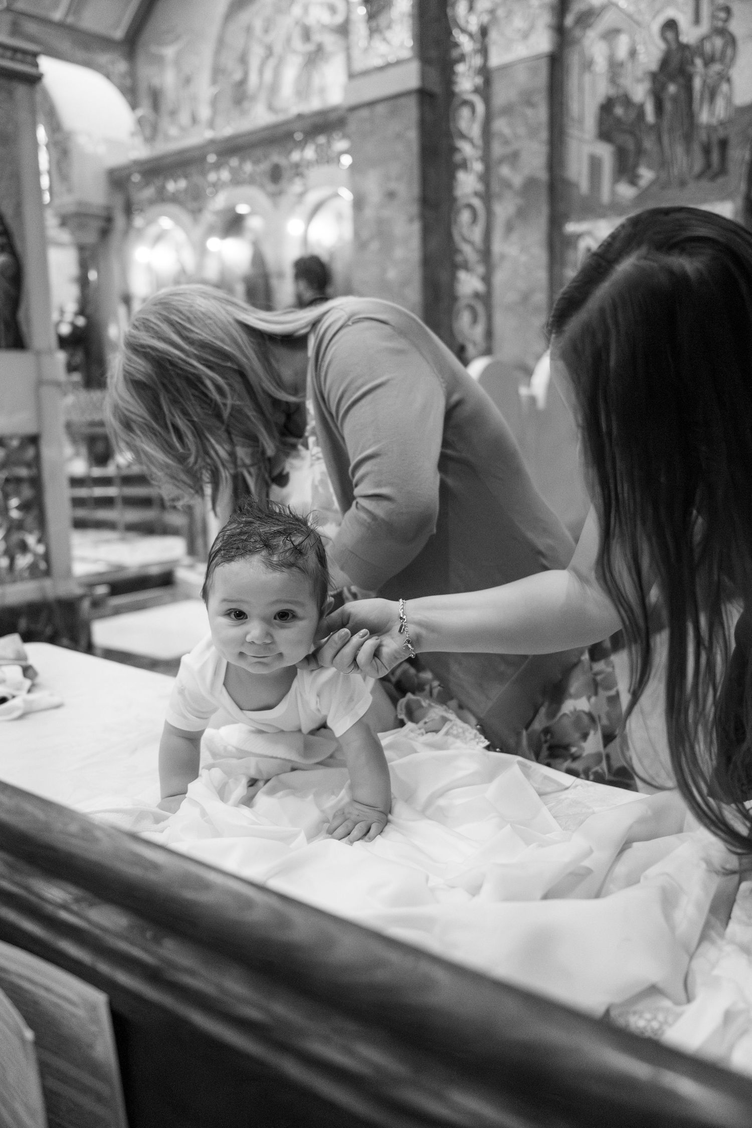 Black and white photos capturing tender moments of a baby's baptism ceremony in a church setting.