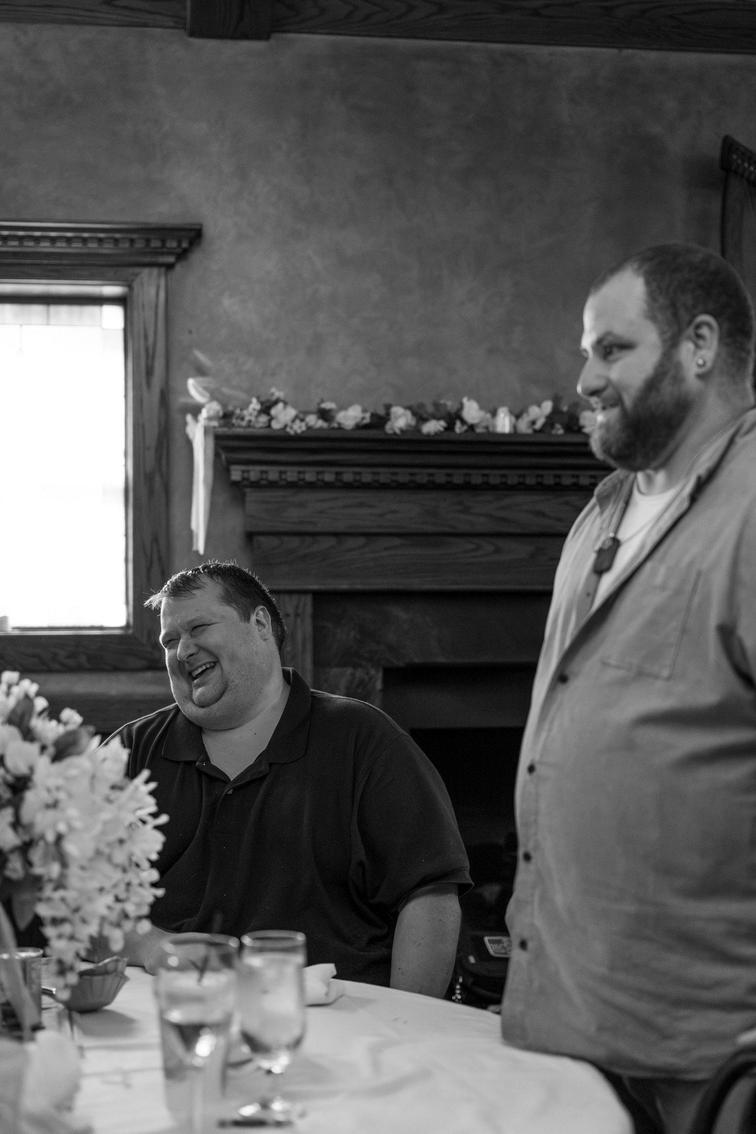 Two people engaged in conversation at a dining table with floral centerpieces and dark wood decor.