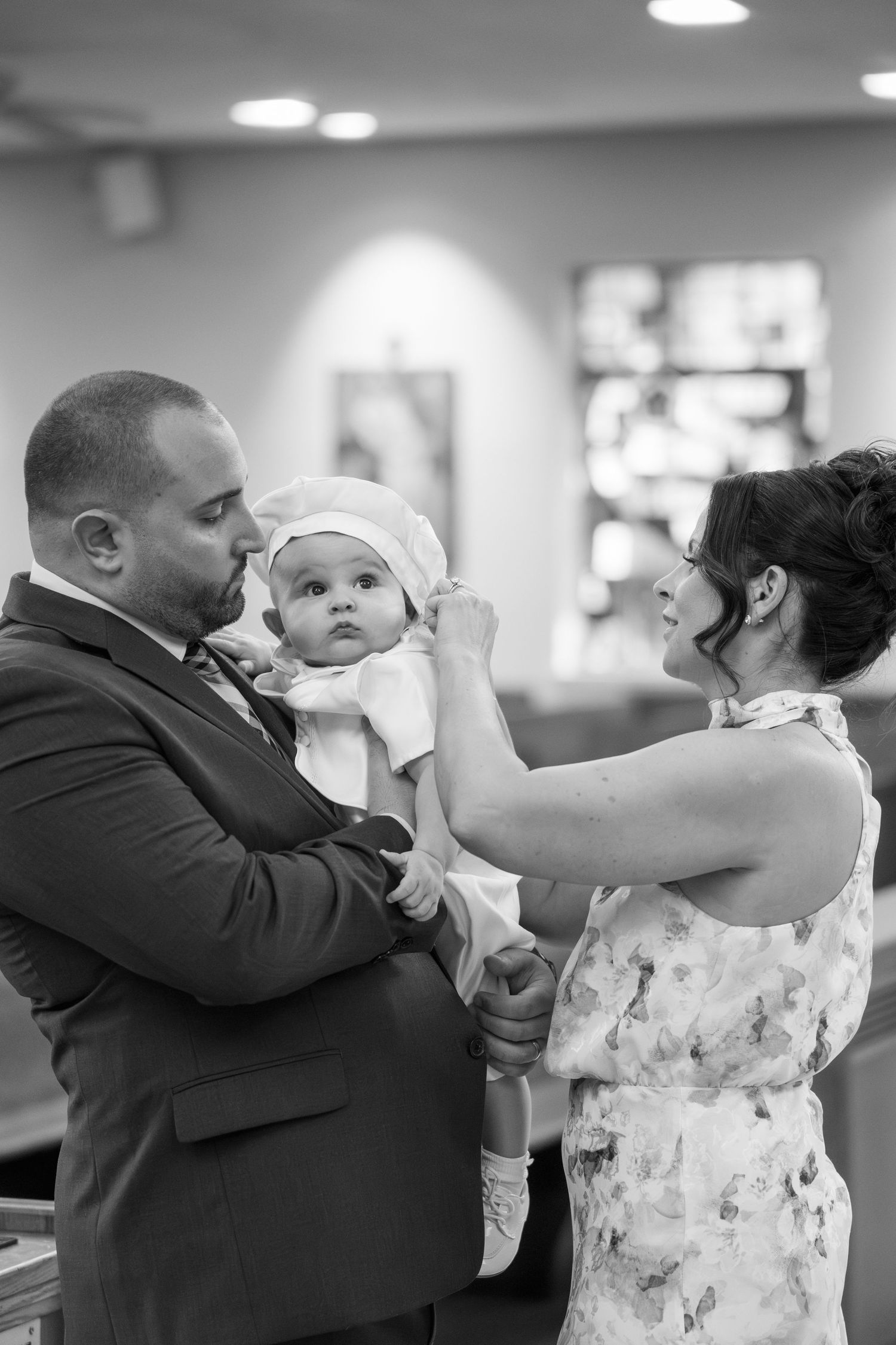 A touching black and white moment during a baptism ceremony as parents adjust their baby's white christening outfit.