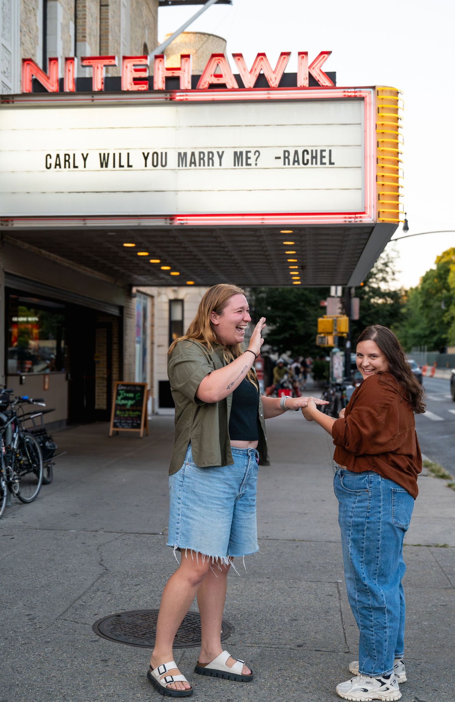 Marquee sign outside of a movie theater with a marriage proposal message displayed in bright letters.