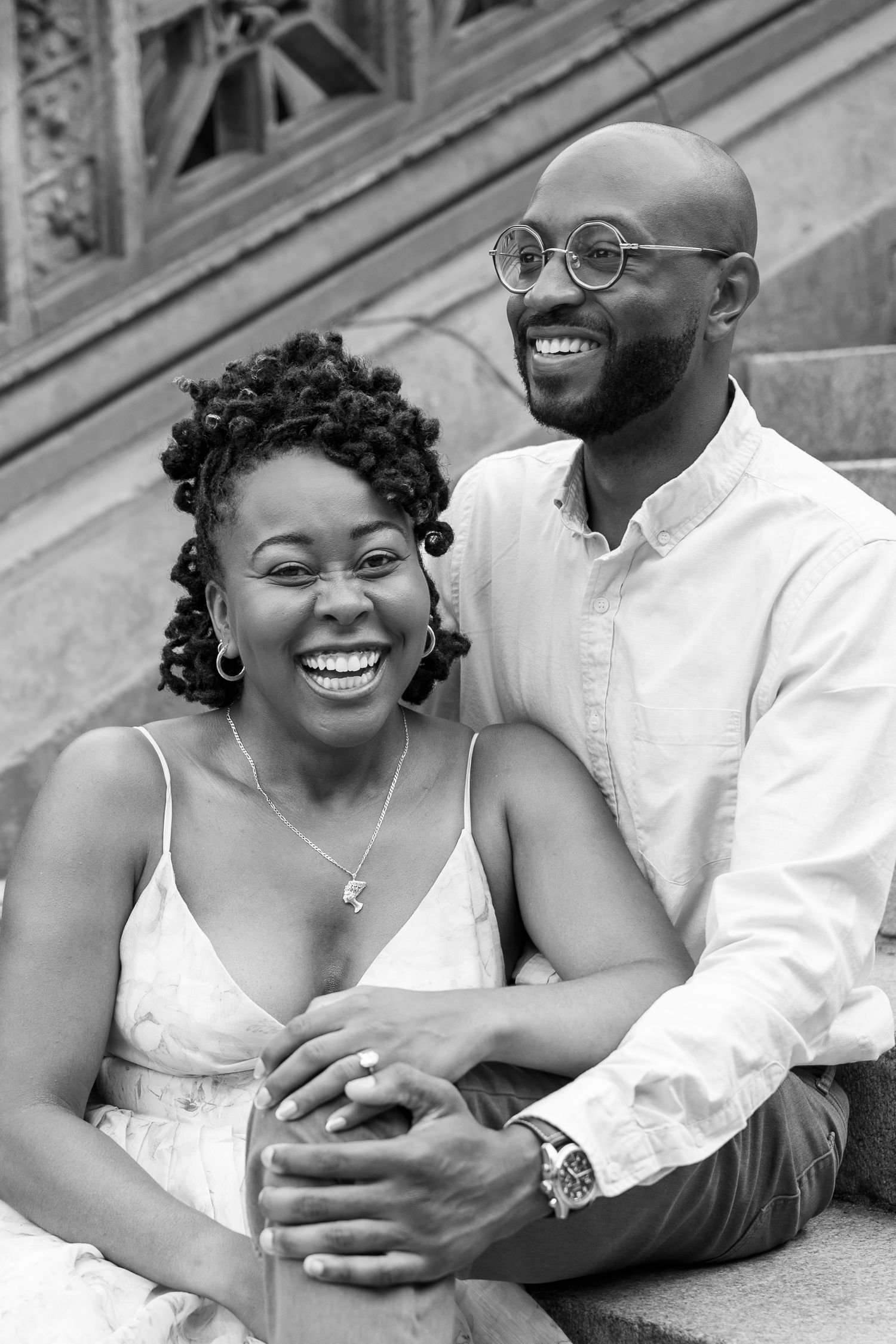 Joyful couple laughing together during engagement photo session on stone steps.