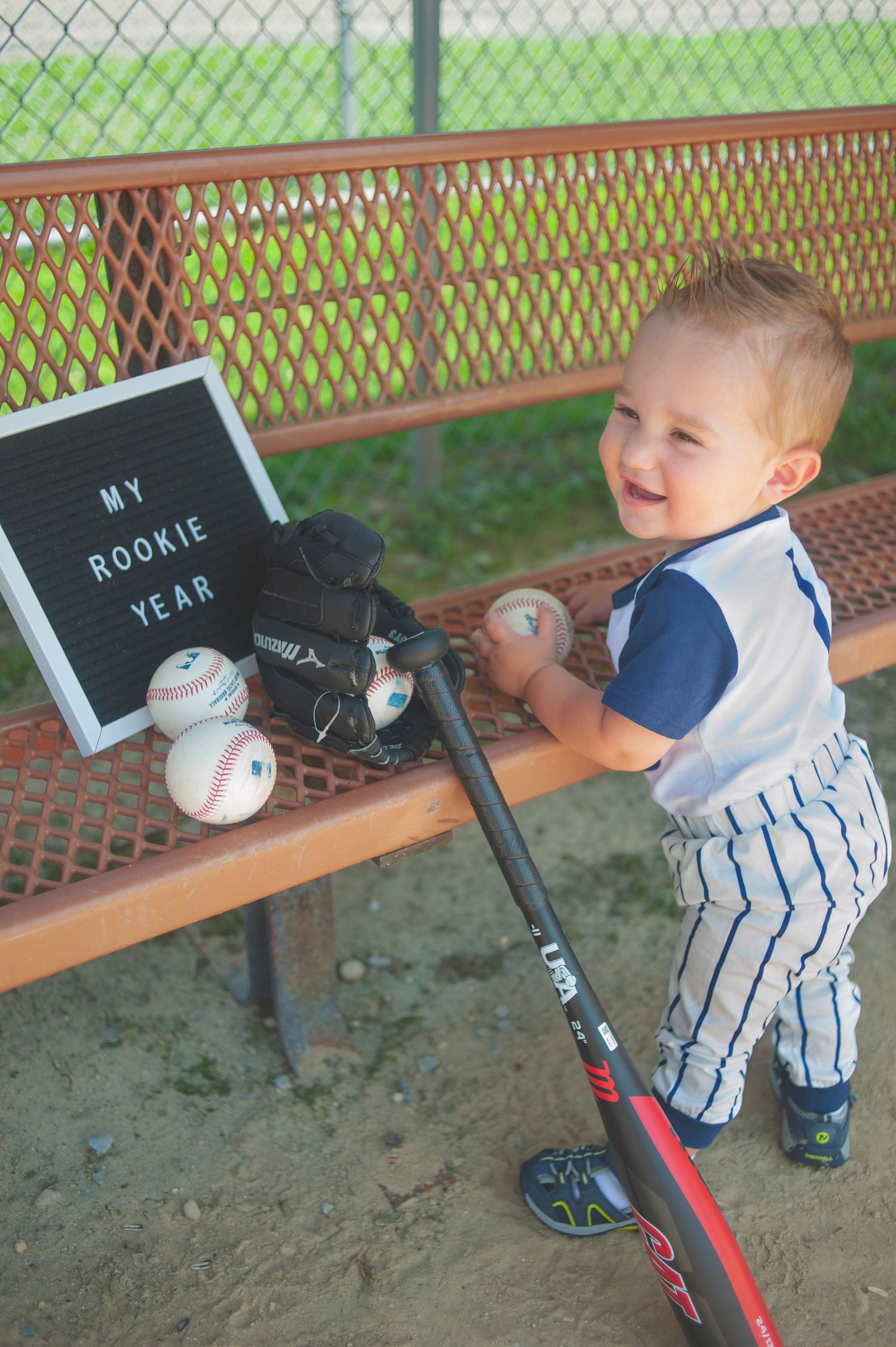 Young baseball player practicing with a tee in pinstripe uniform on a baseball field.