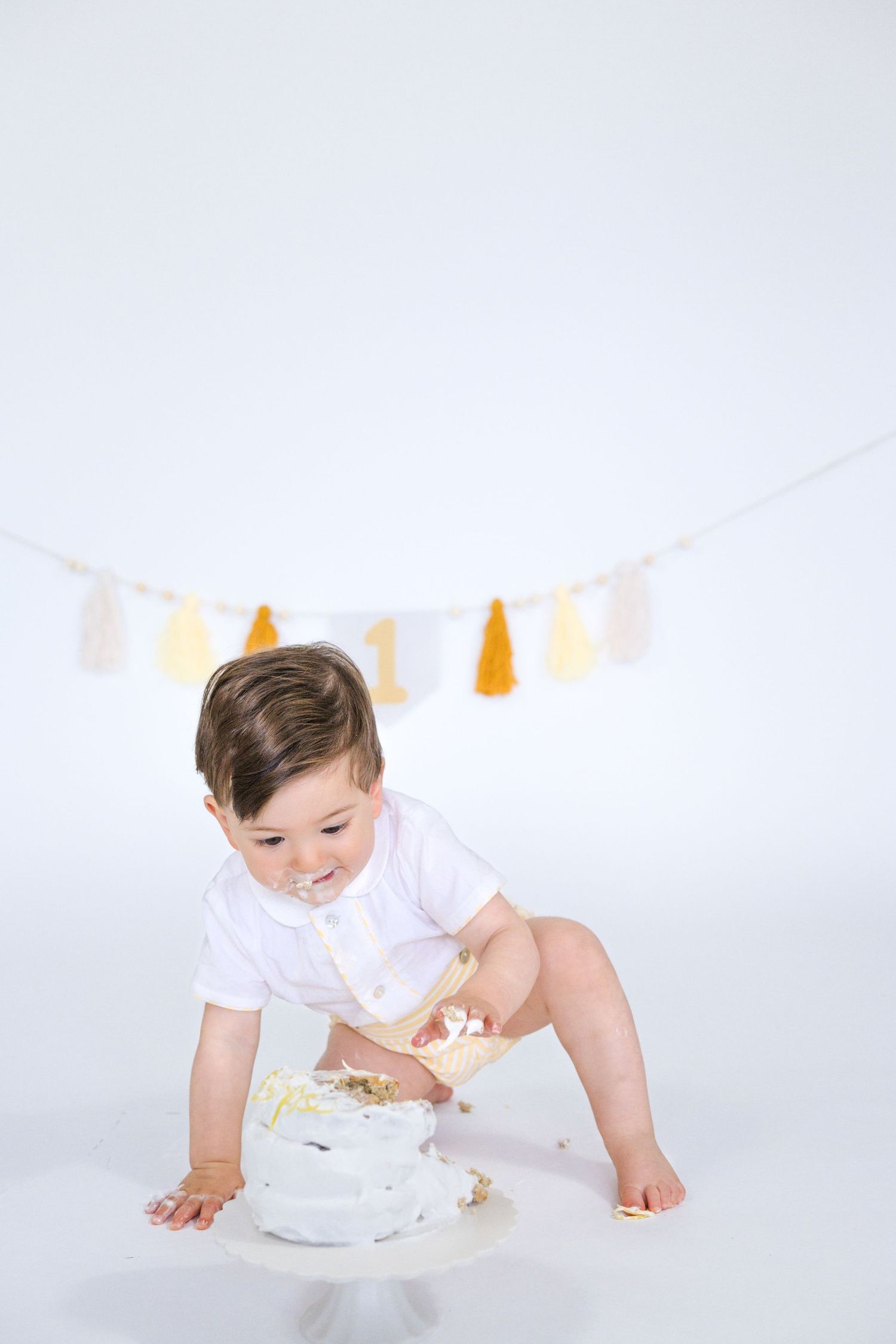 Baby crawls towards white birthday cake during first birthday photo shoot.