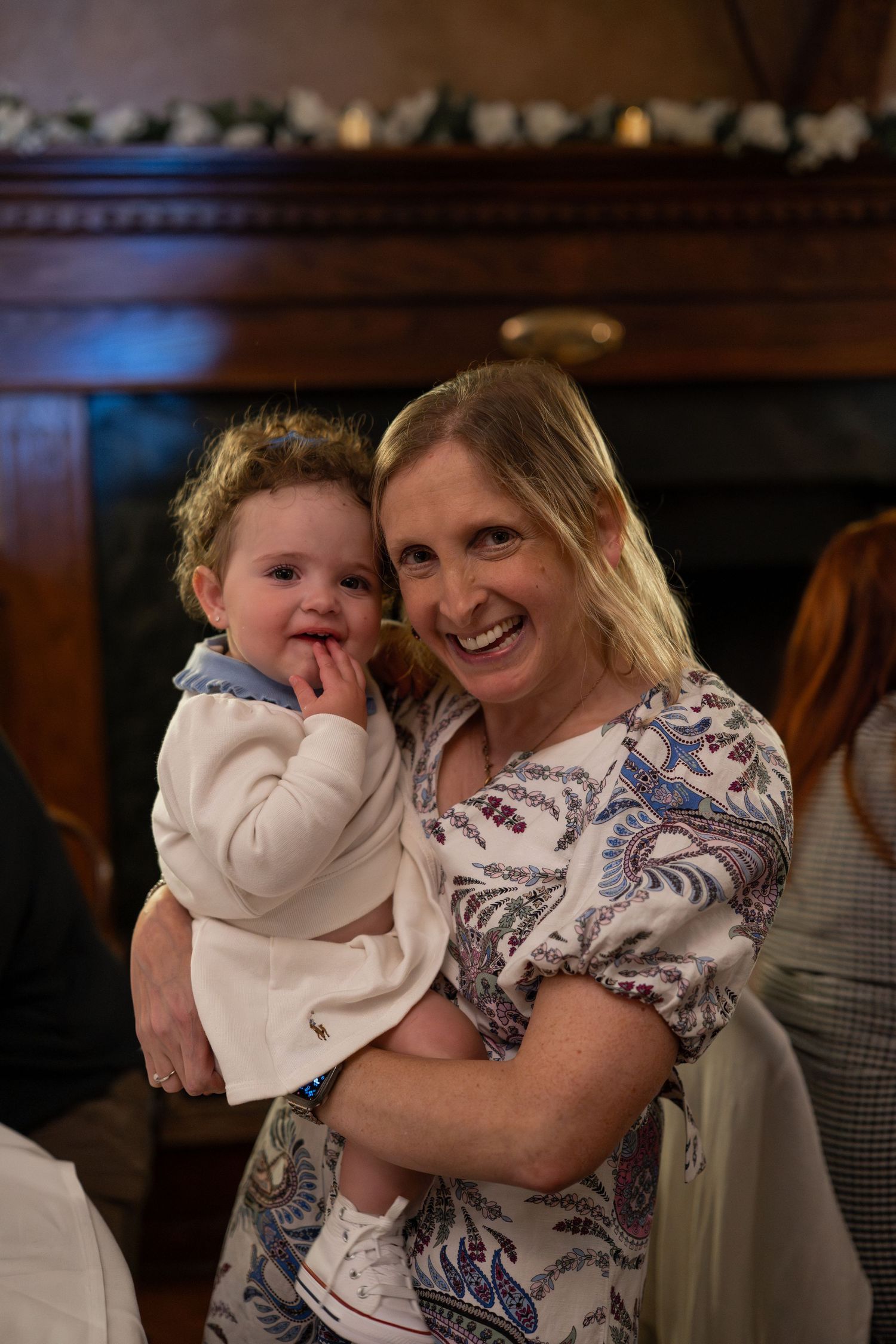 A baby in white clothing is held and cuddled in a dimly lit indoor setting.