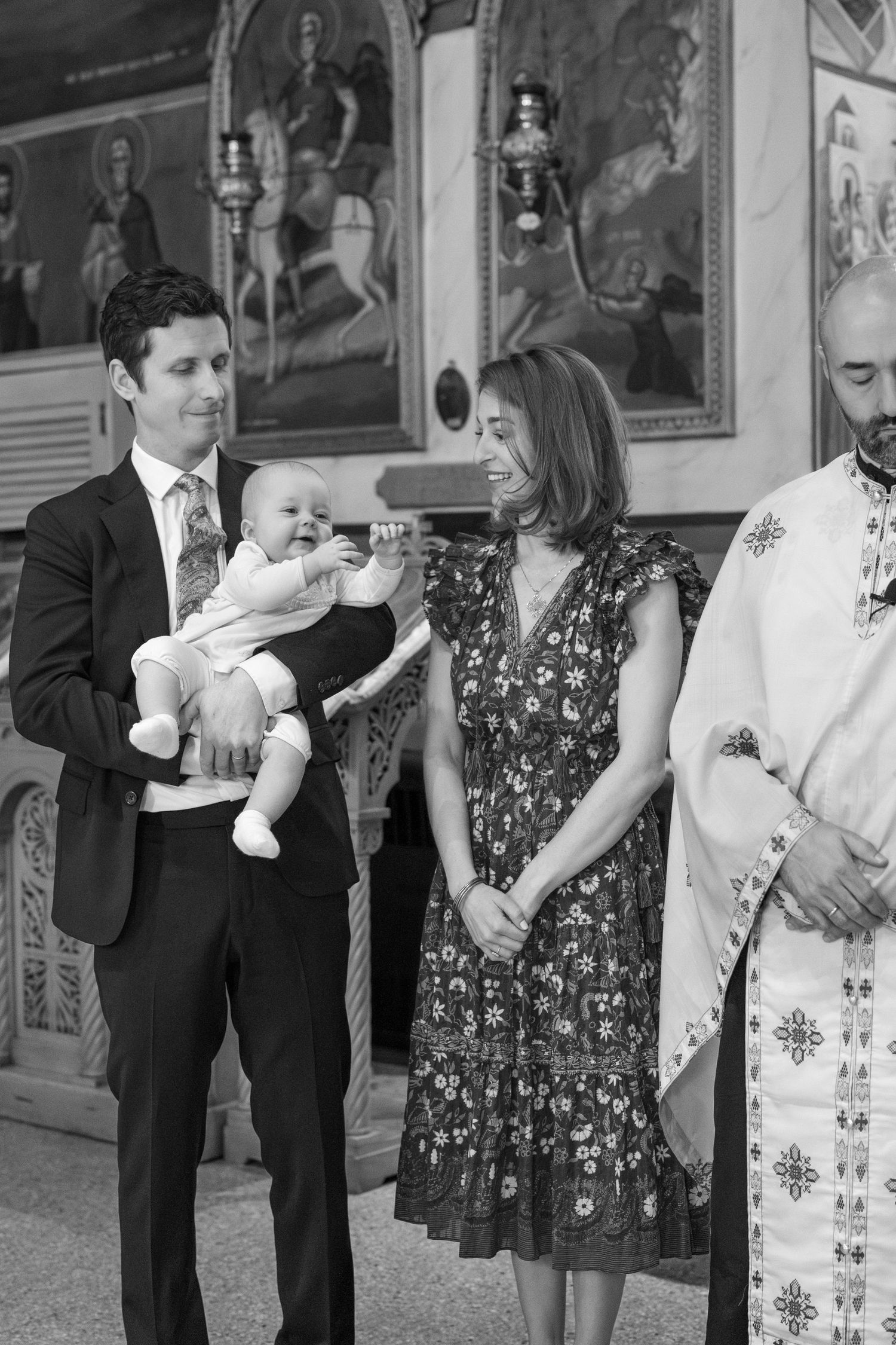 People in formal dress gather for a special ceremony inside a church decorated with religious artwork.