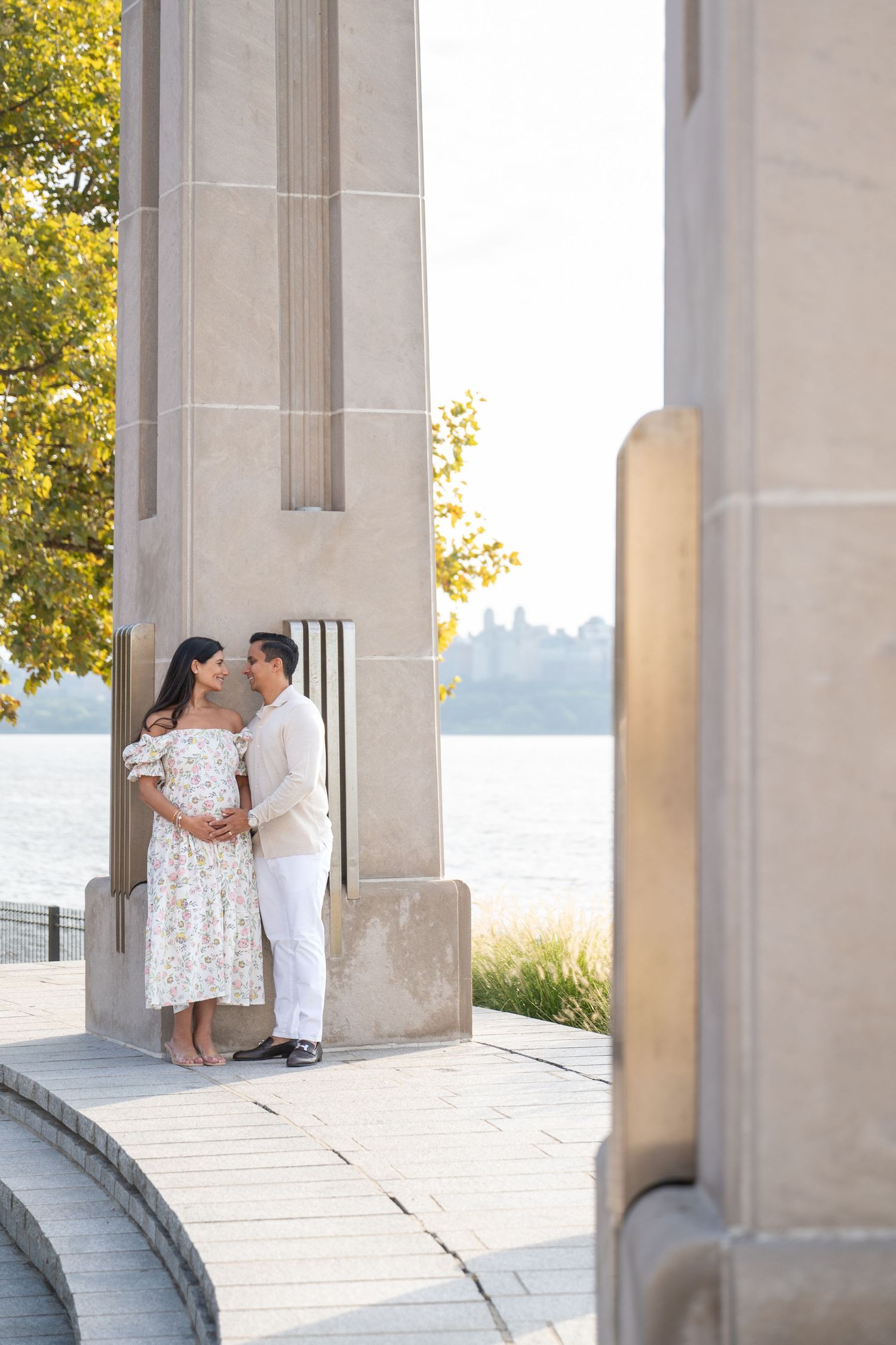 A couple embraces near stone pillars with waterfront views during golden hour.