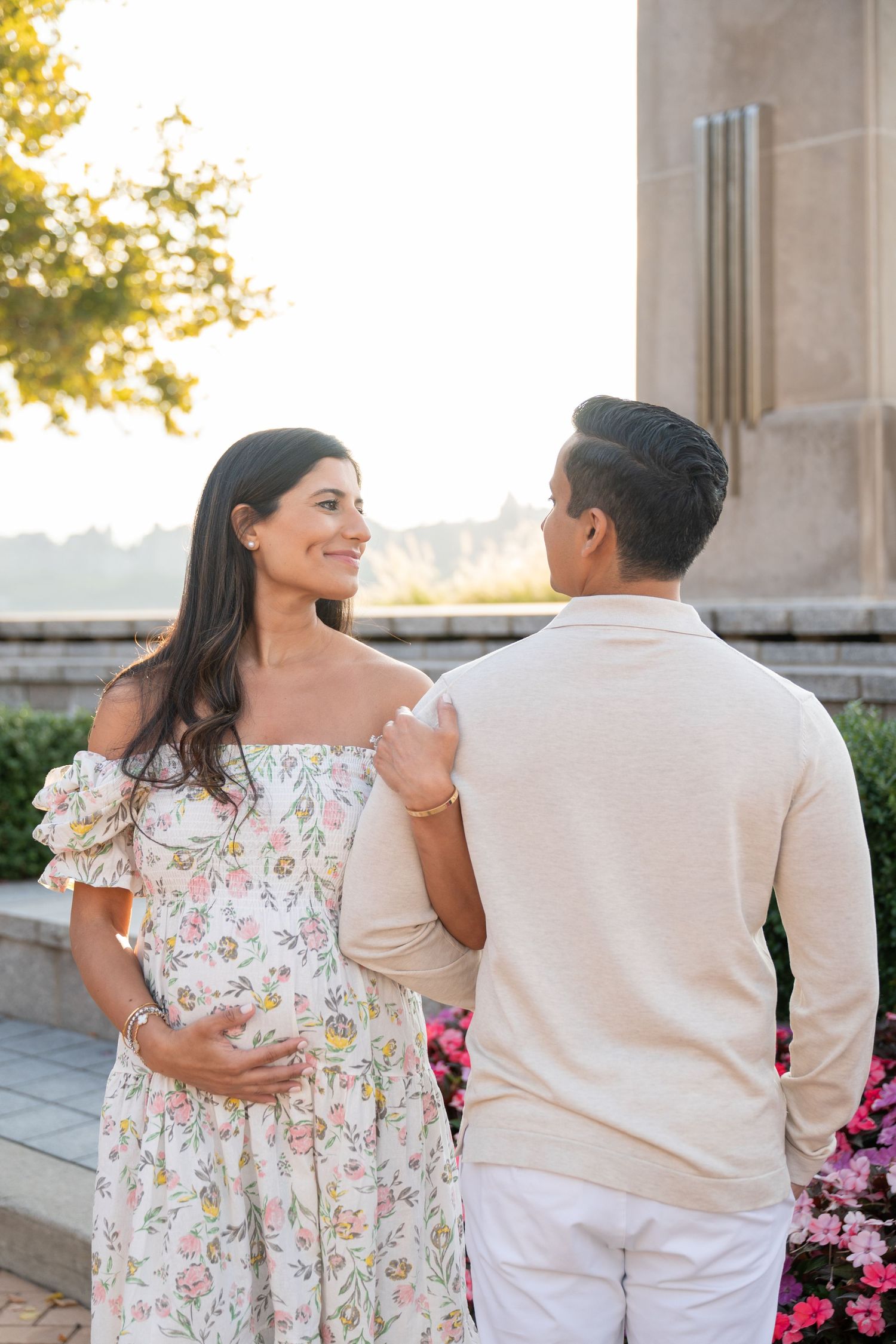 A romantic couple laughs together in a scenic outdoor setting with stone columns and flowers.