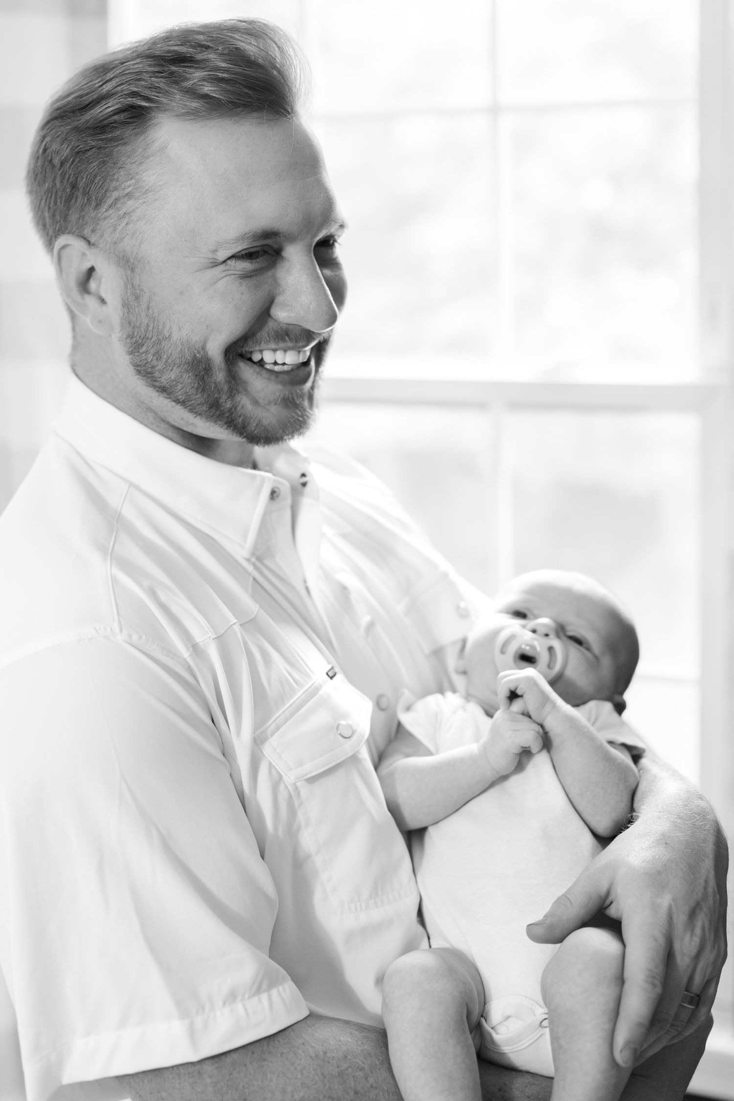 Tender moment captured in black and white of parent cradling newborn in white clothing.