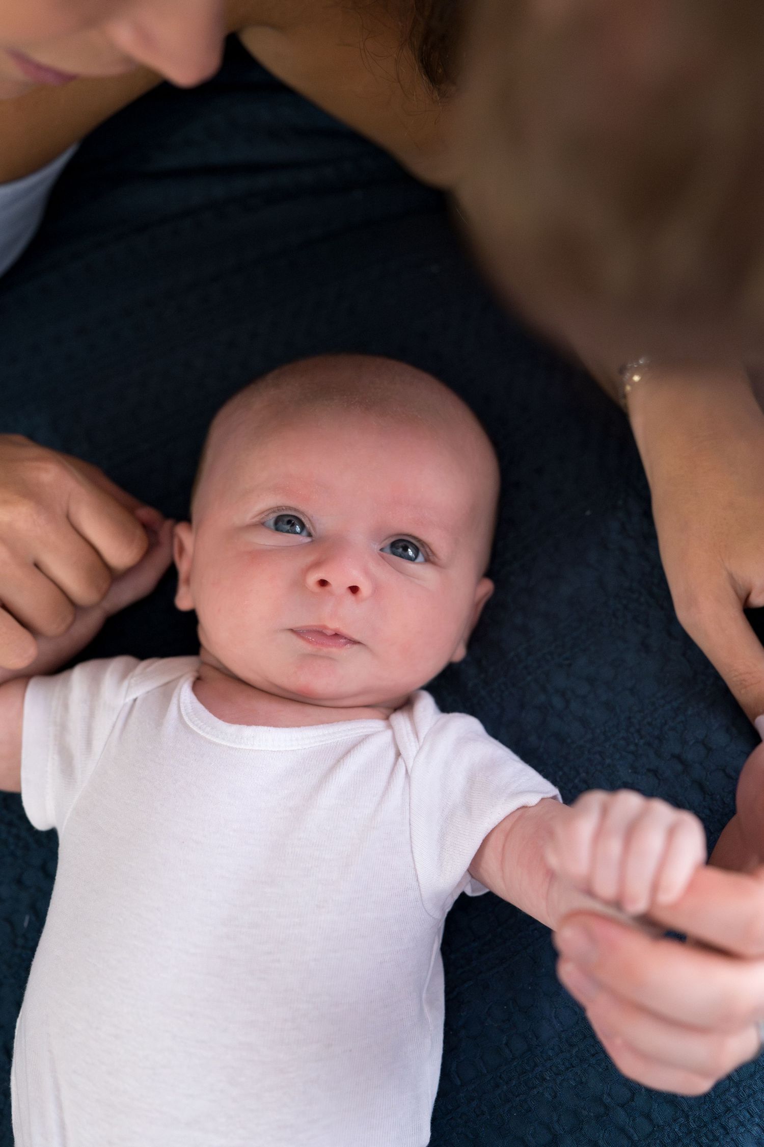 Close-up view of an infant wearing a white onesie lying on dark fabric.